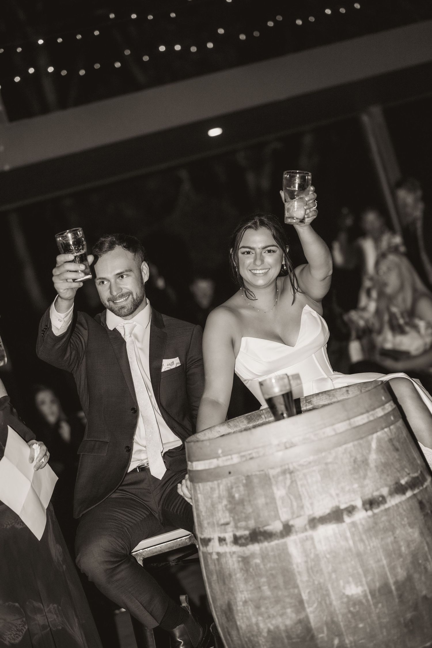 Wedding party guests sitting in rustic wooden barrels during a fun reception moment.