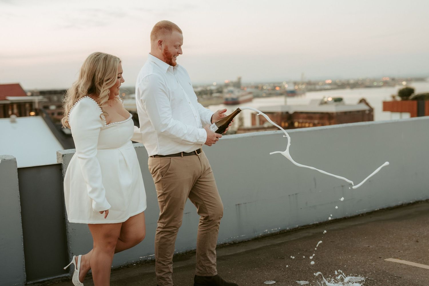 A couple stands on a rooftop terrace overlooking a scenic cityscape during golden hour.