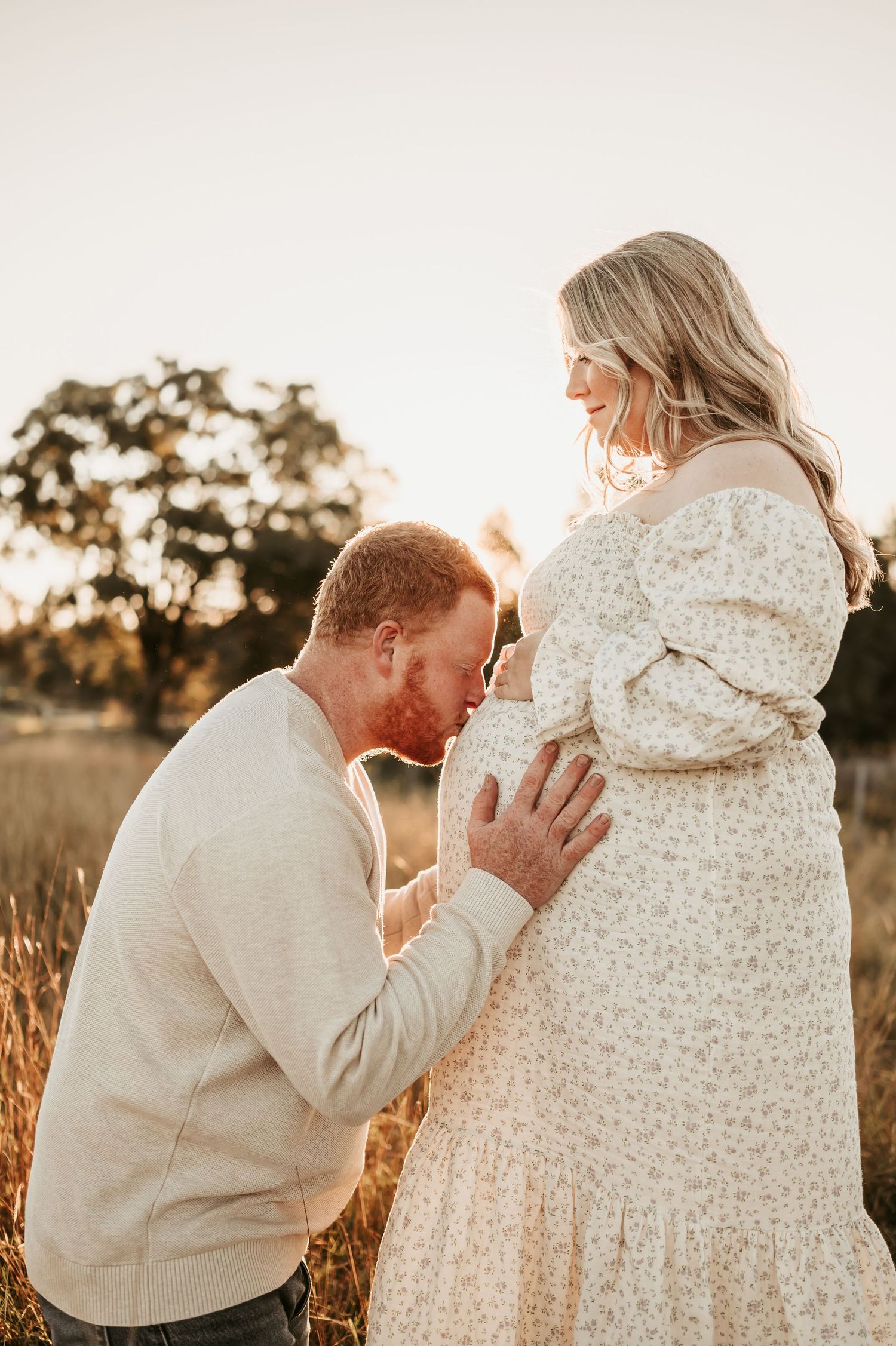 Intimate maternity moment captured in a field at golden hour with gentle touches.