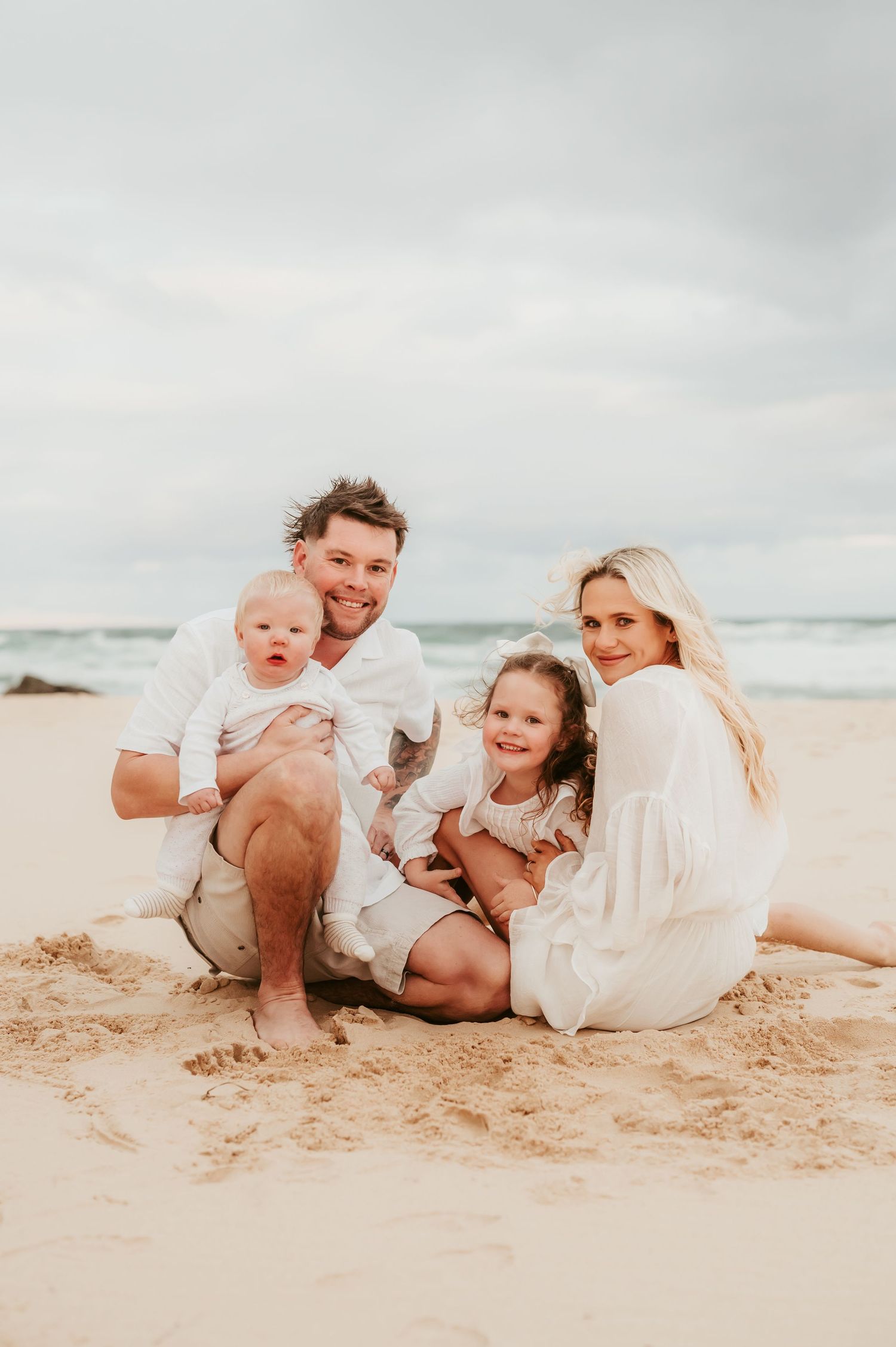 A family sits together on a sandy beach during golden hour.