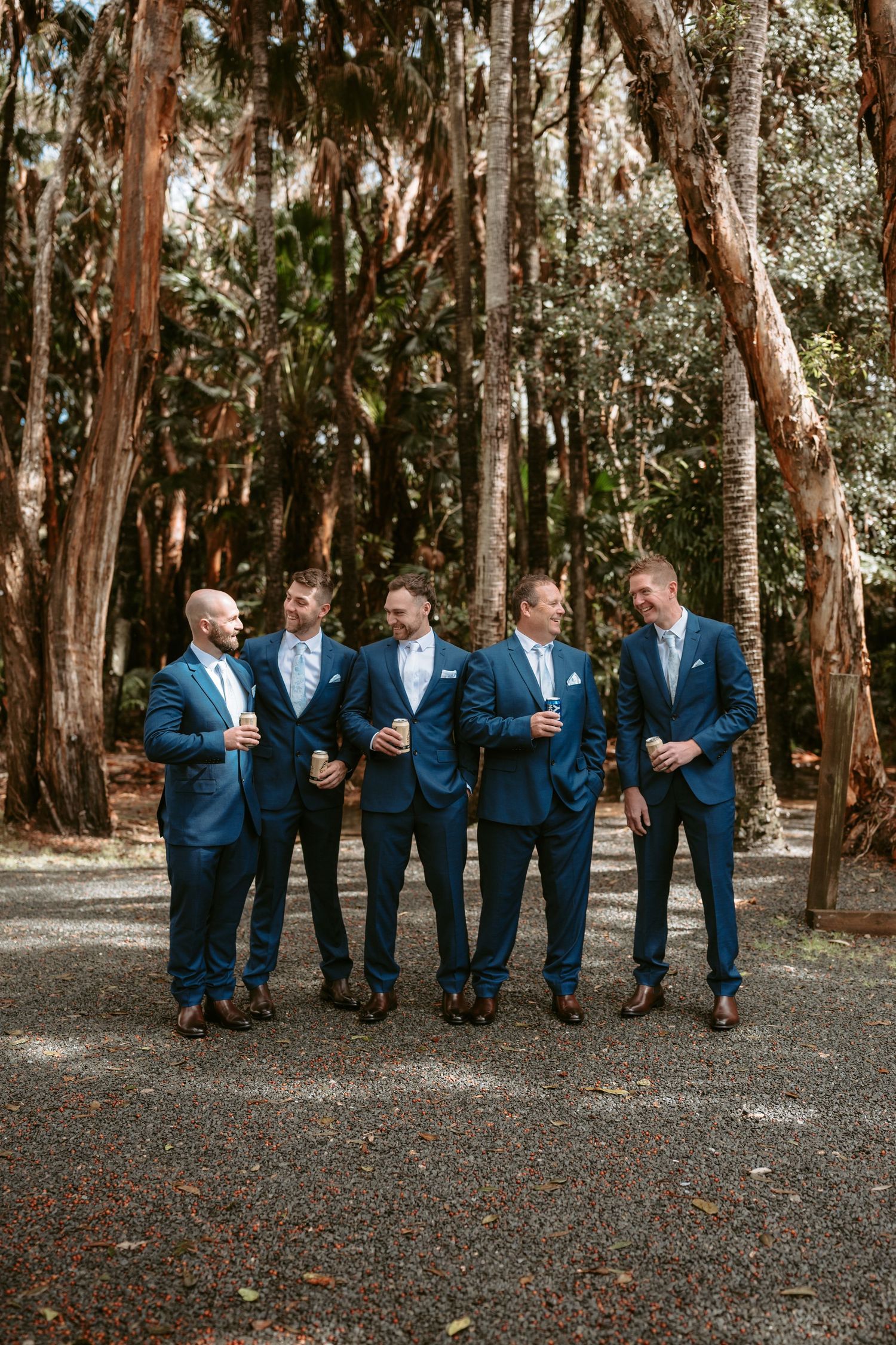 Groomsmen in matching navy suits posing together in a wooded outdoor setting.