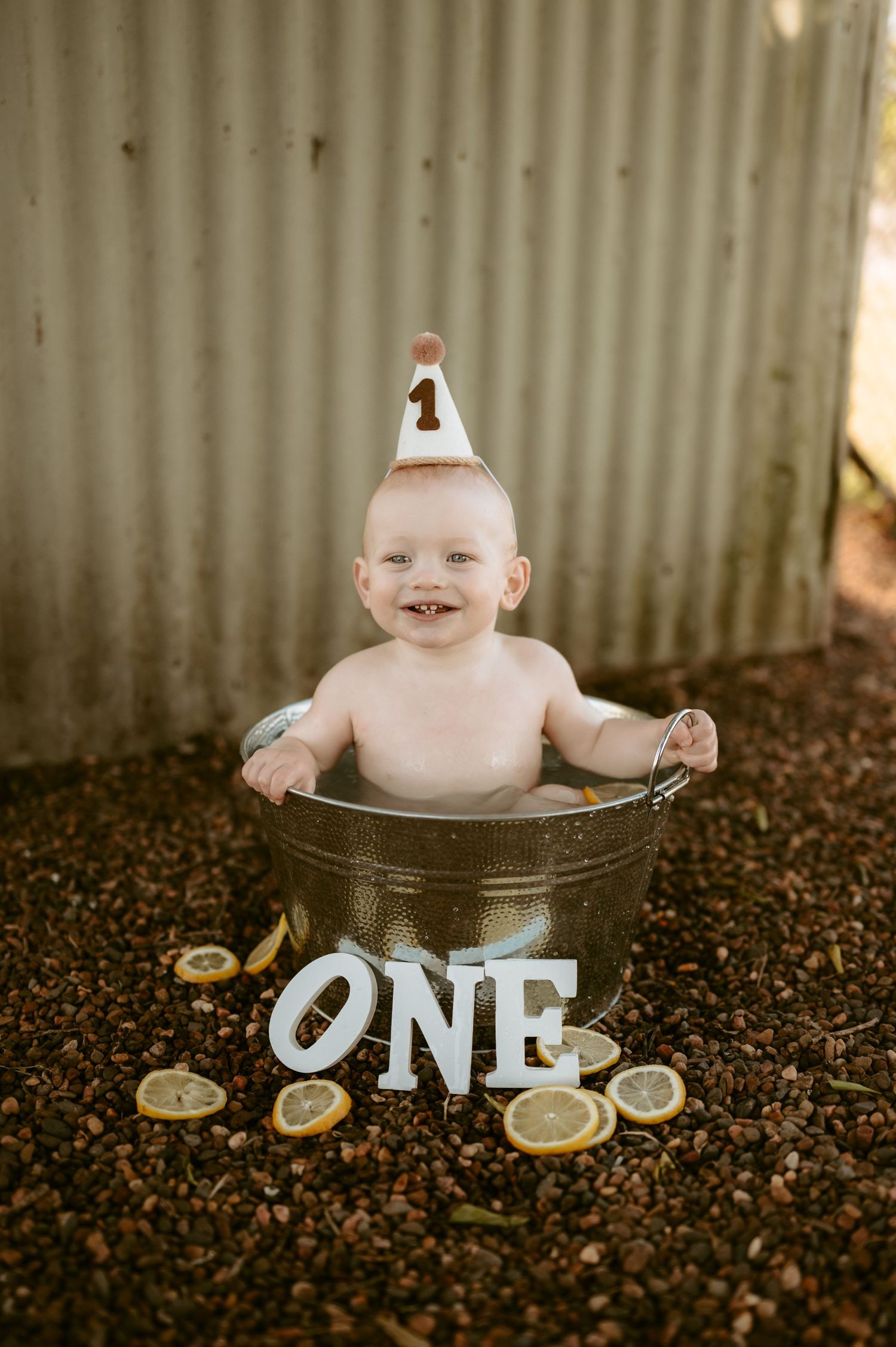 Baby sitting in rustic metal tub with 'ONE' letters and party decorations.
