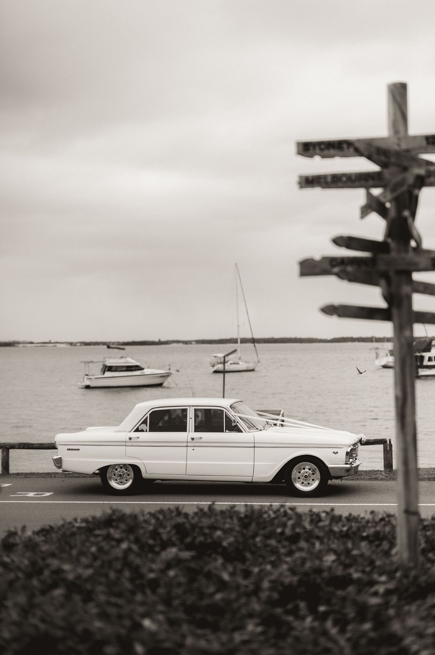 Classic vintage white car parked along waterfront in black and white photography.