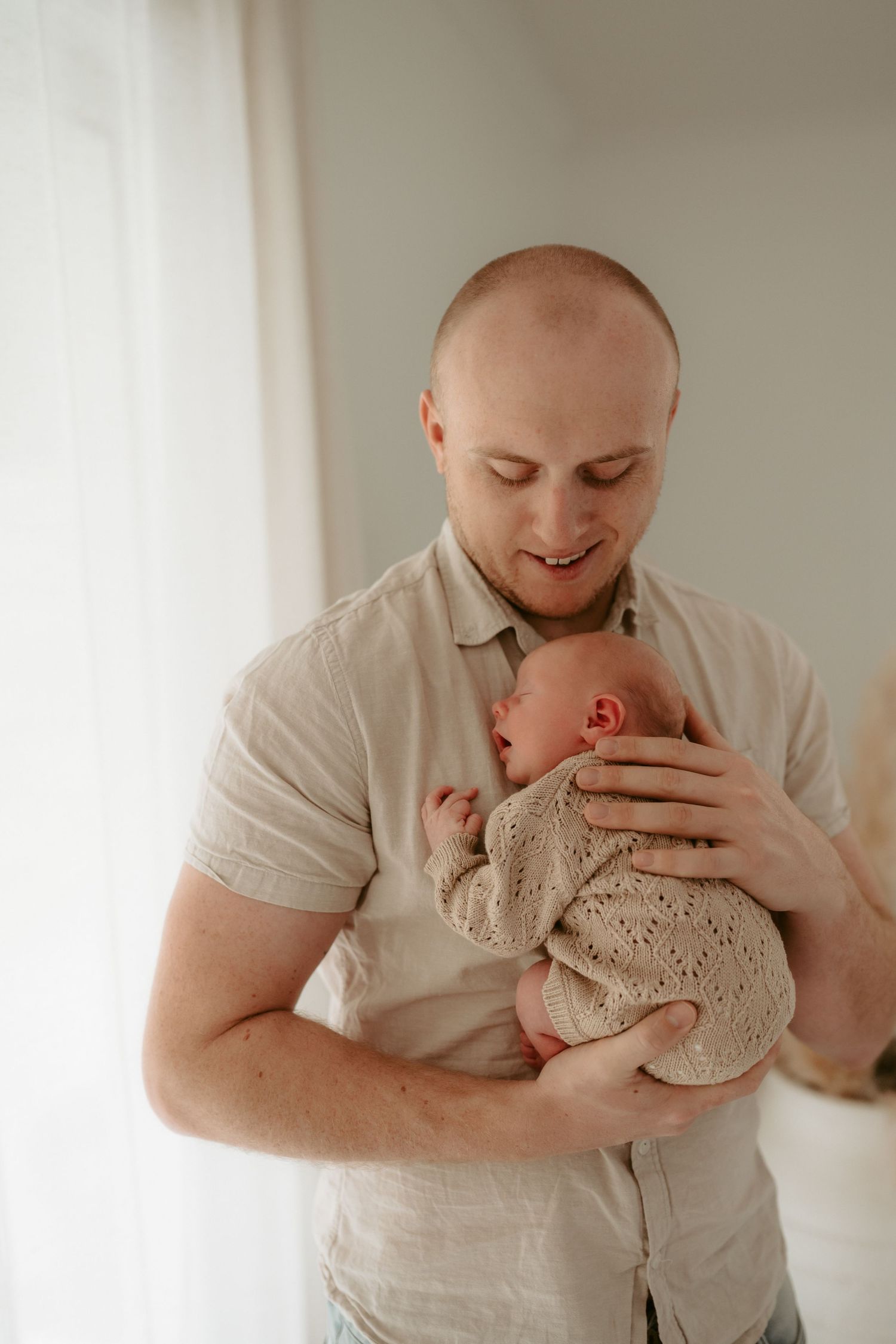 A gentle moment as a father cradles a sleeping newborn in a light-filled room.