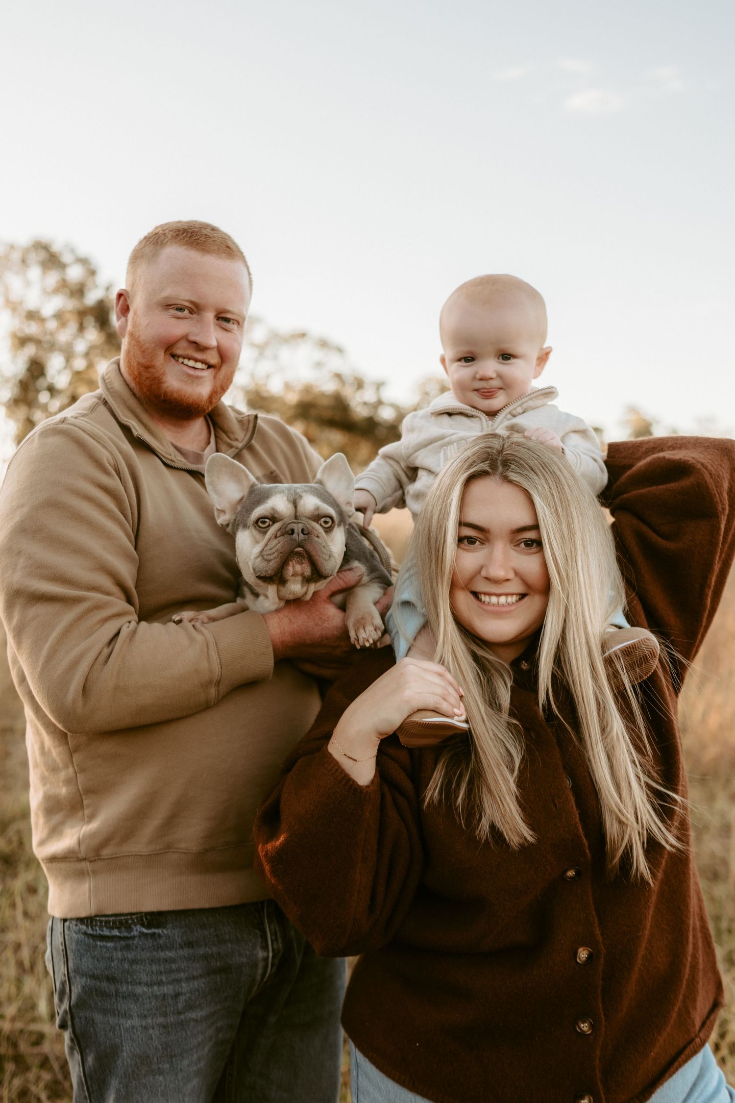 Family portrait with a small dog and child in warm autumn lighting.