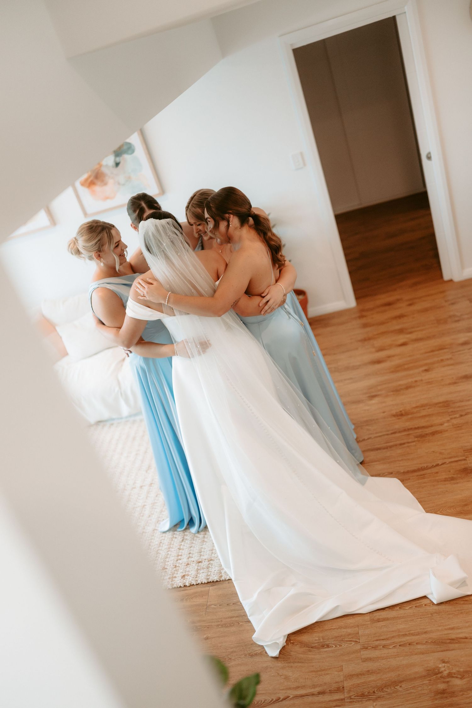 Bridesmaids in light blue dresses helping with wedding dress preparations.
