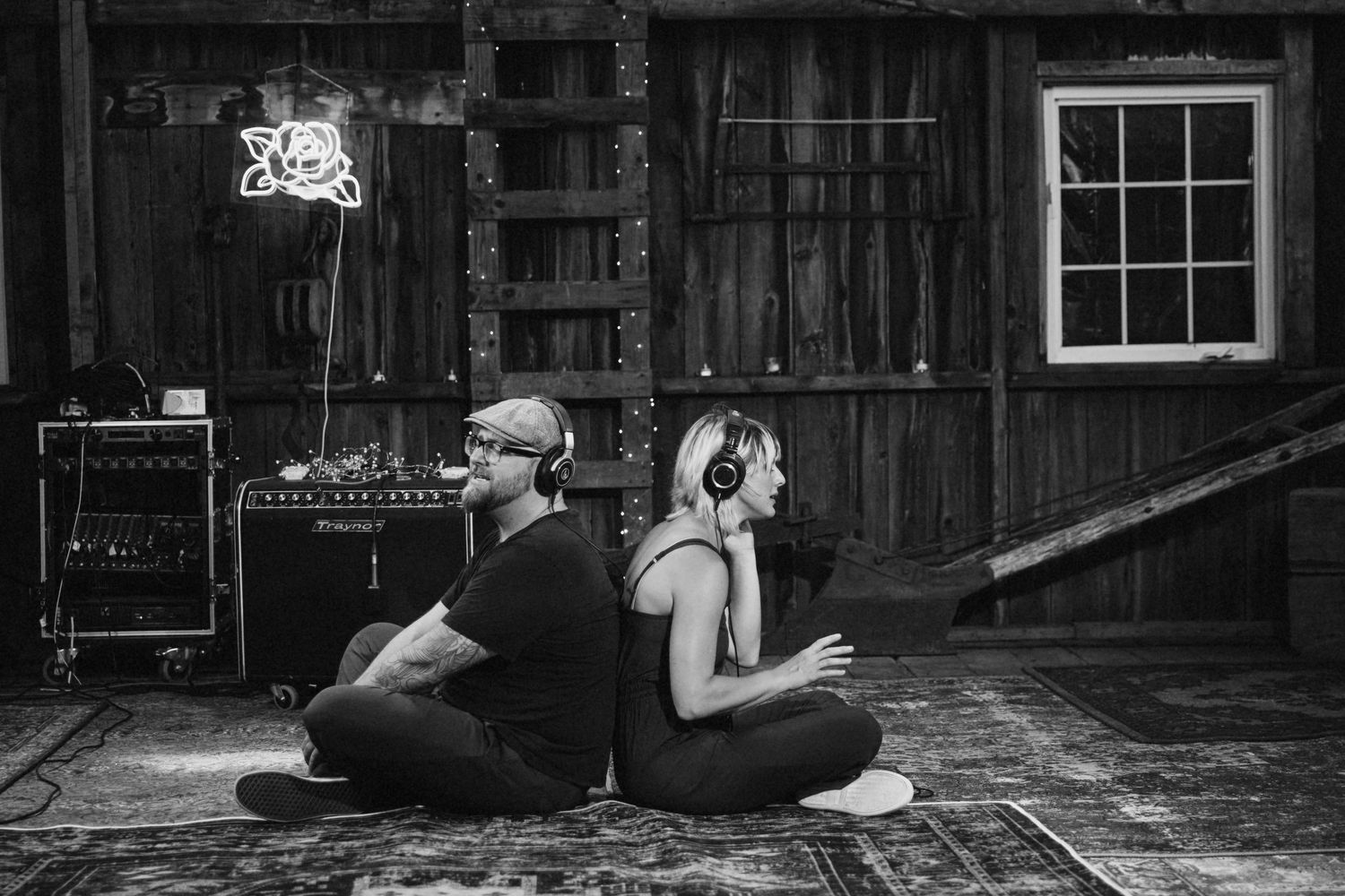 Photo of two band members singing with headphones on, back to back.