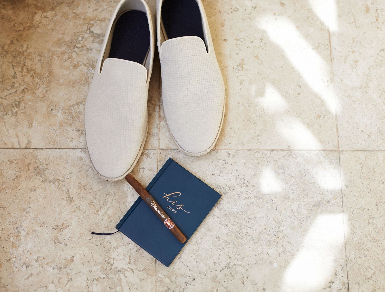Grooms shoes, cigar and vow book with sunlight shining on floor.