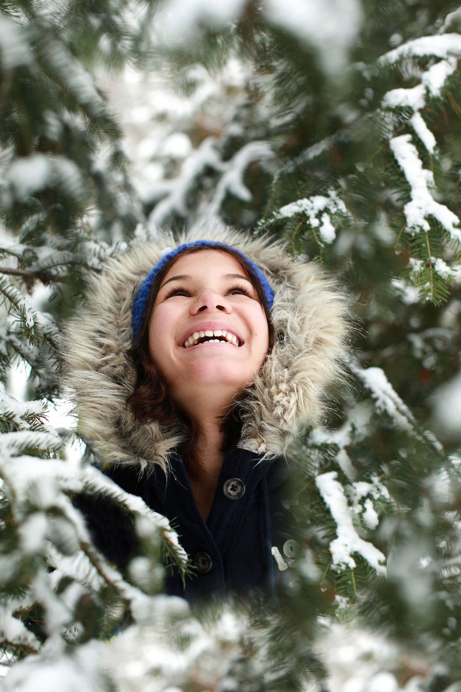 Photo of a child in a group of snow covered trees, looking up at the sky in wonder.
