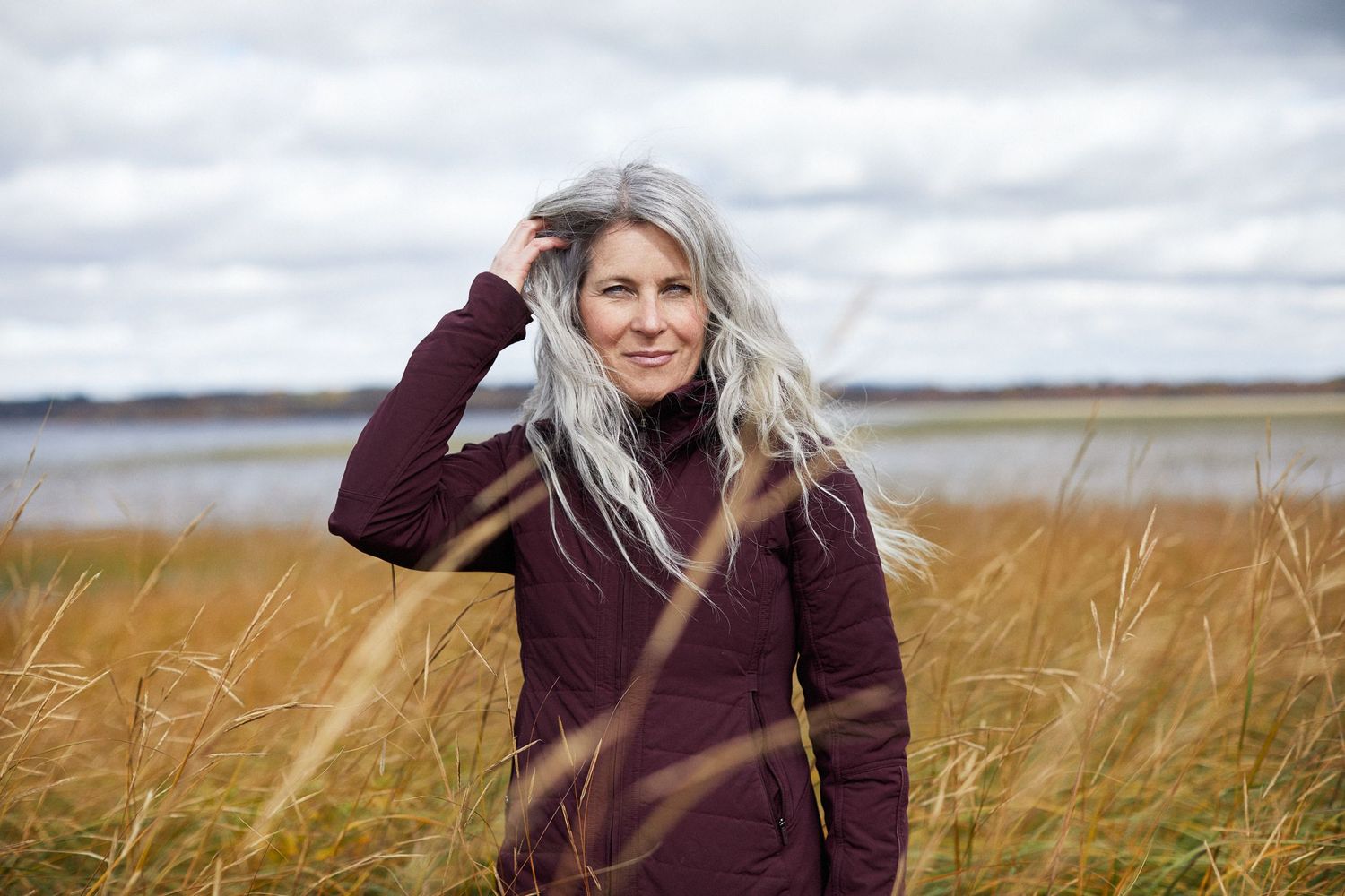 Portrait of a woman with long grey hair in a field with long grass.