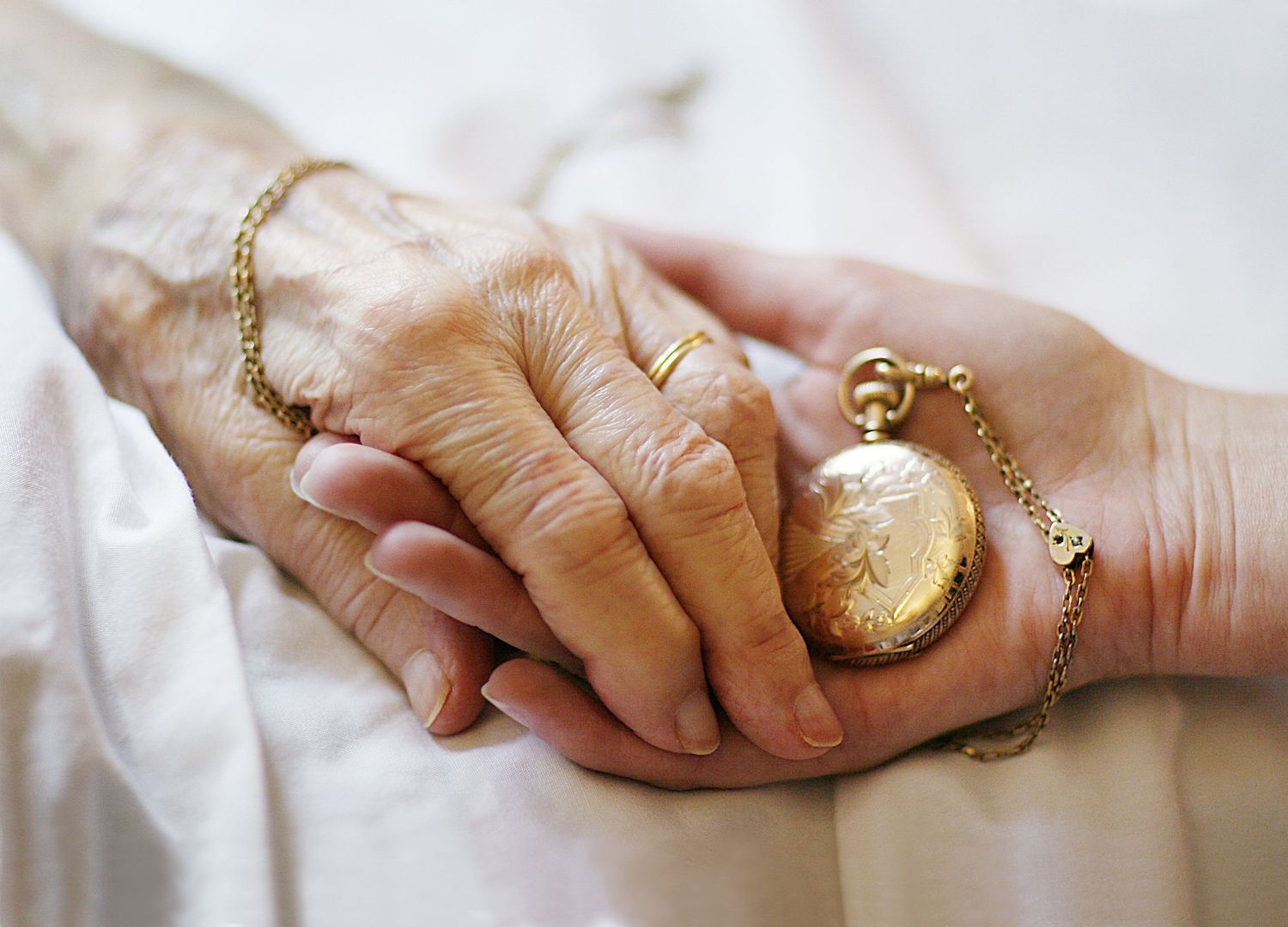 Photo of an elderly hand holding a young one  with a pocket watch in their hands.
