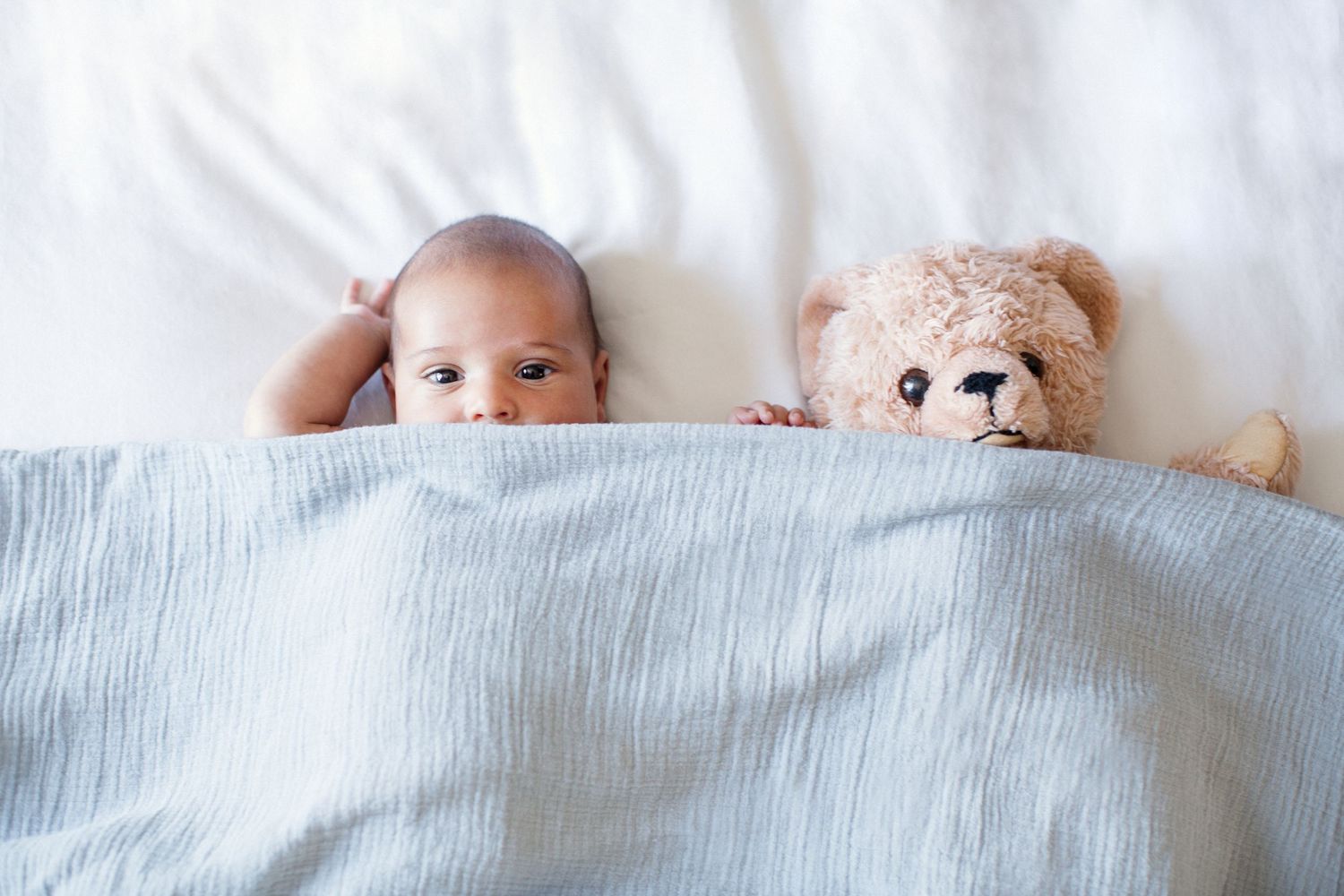 Baby and tedding bear tucked into bed.