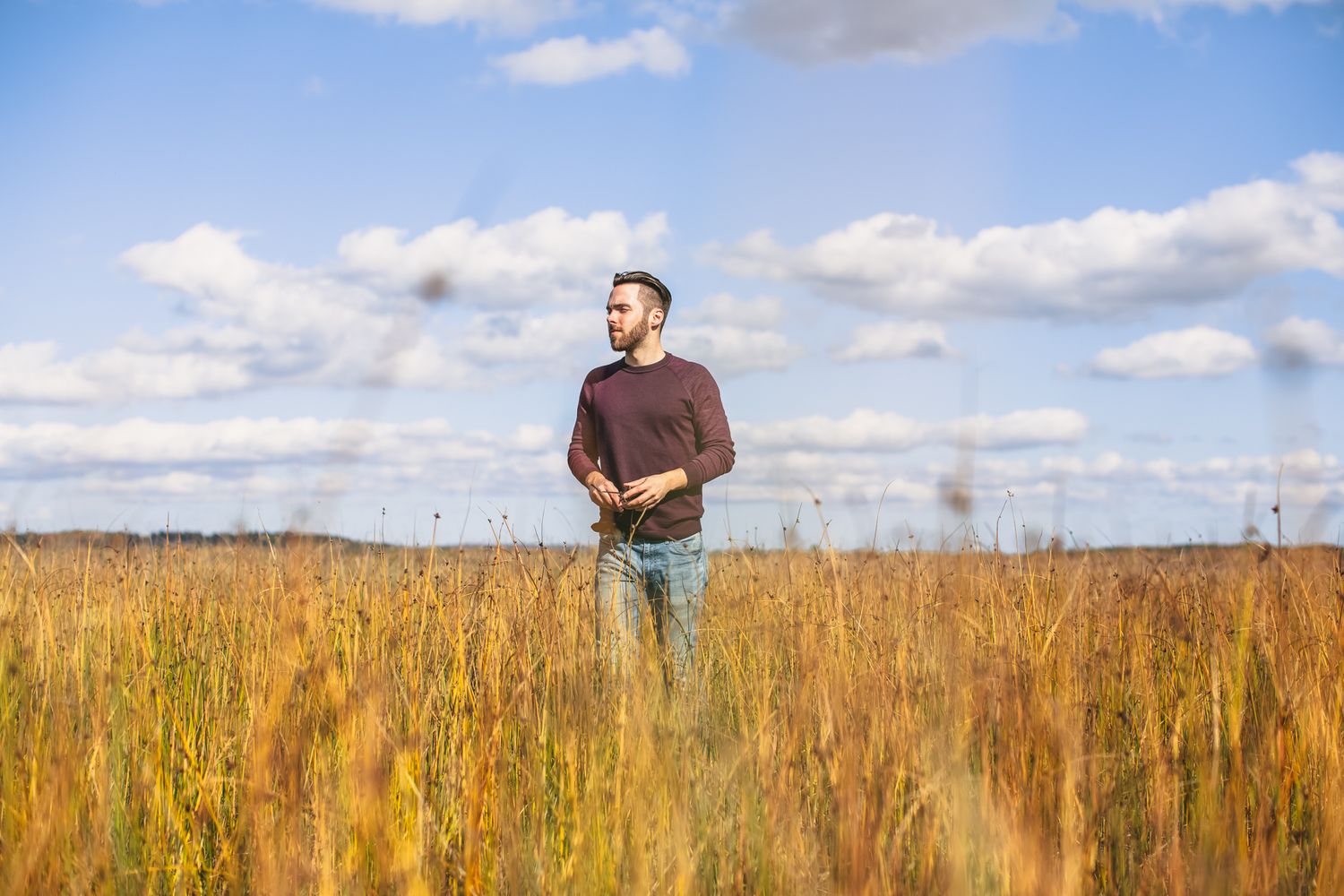 Photograph of a young man walking in a field of tall grass.