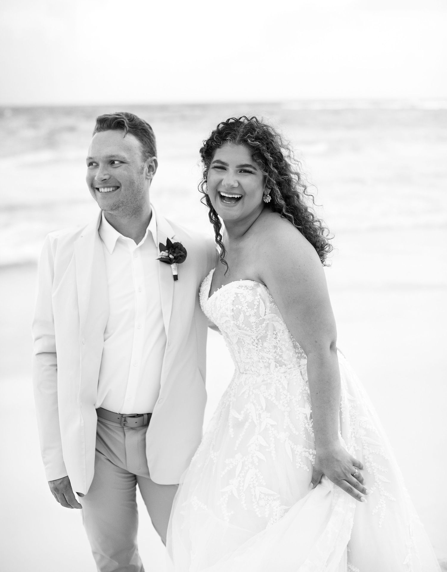 Bride and groom laughing and posing by the ocean.
