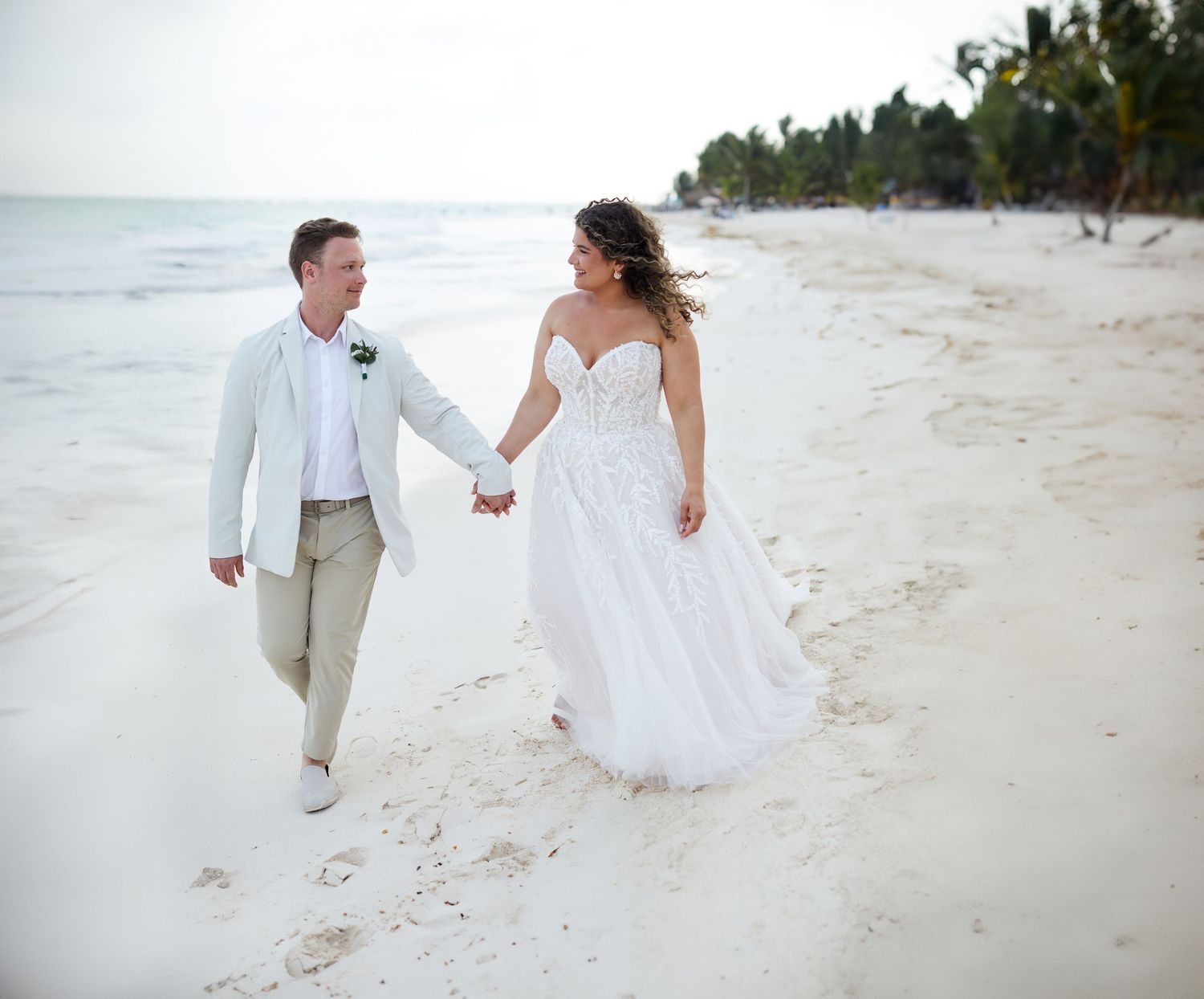 Bride and groom walking on the beach and holding hands.