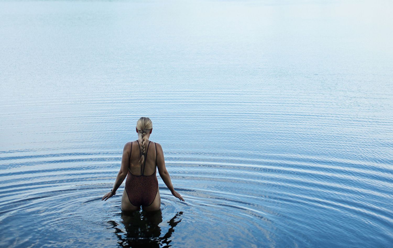 Photo of a woman entering a calm and serene lake.