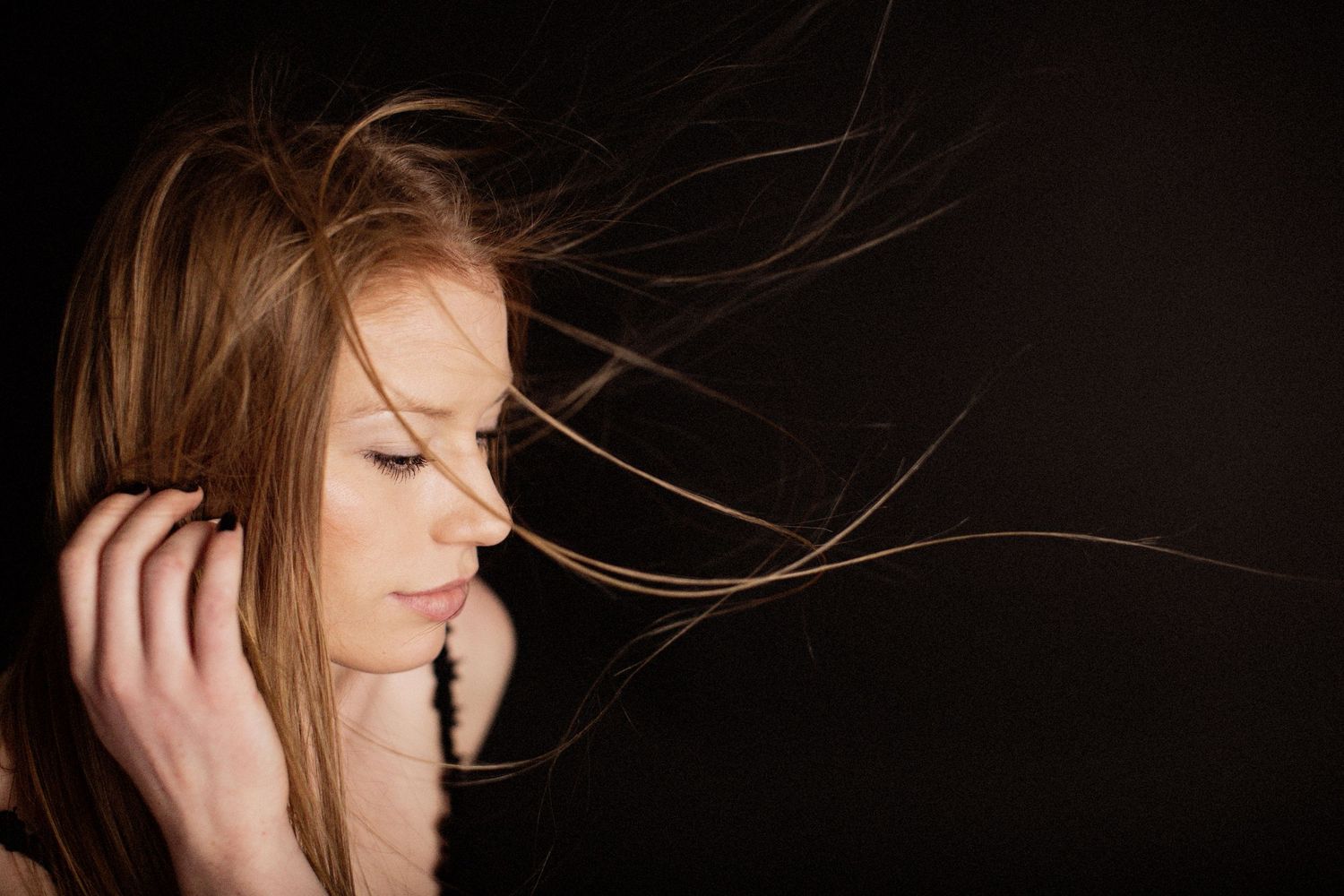 Model against black backdrop with hair blowing.