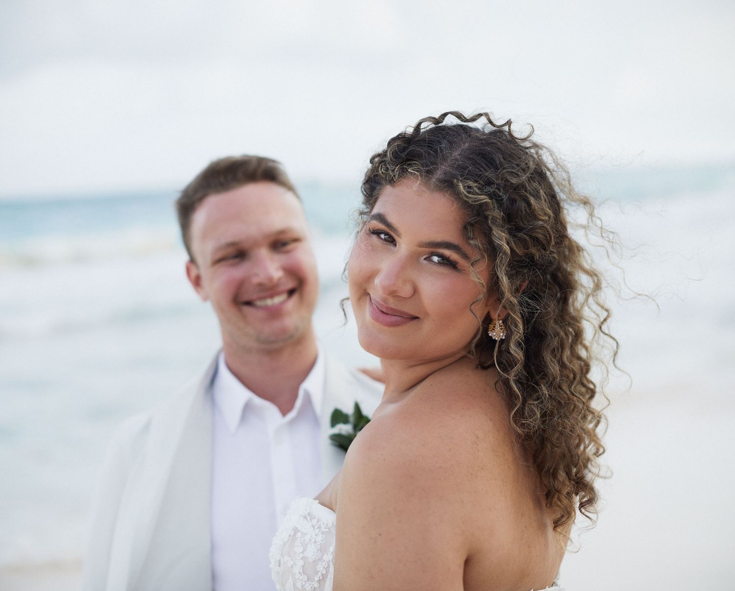 Wedding photo of bride looking into camera and husband looking at her, lovingly.