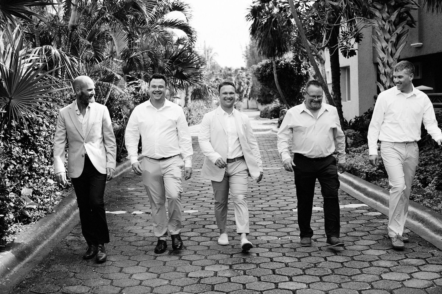 Groom and male wedding participants walking together towards camera and laughing.