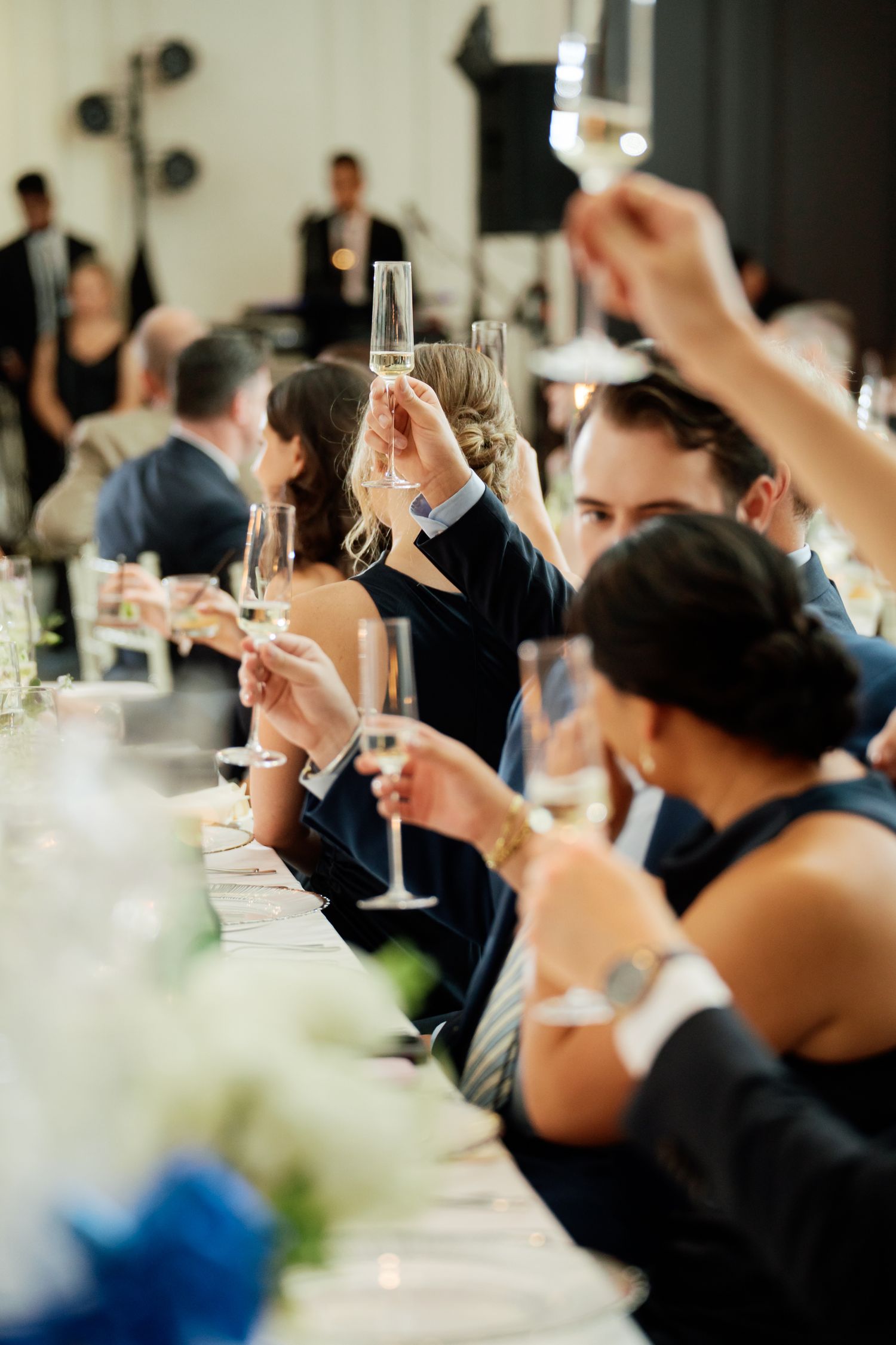 Guests raising champagne glasses in a toast at an elegant wedding reception dinner.