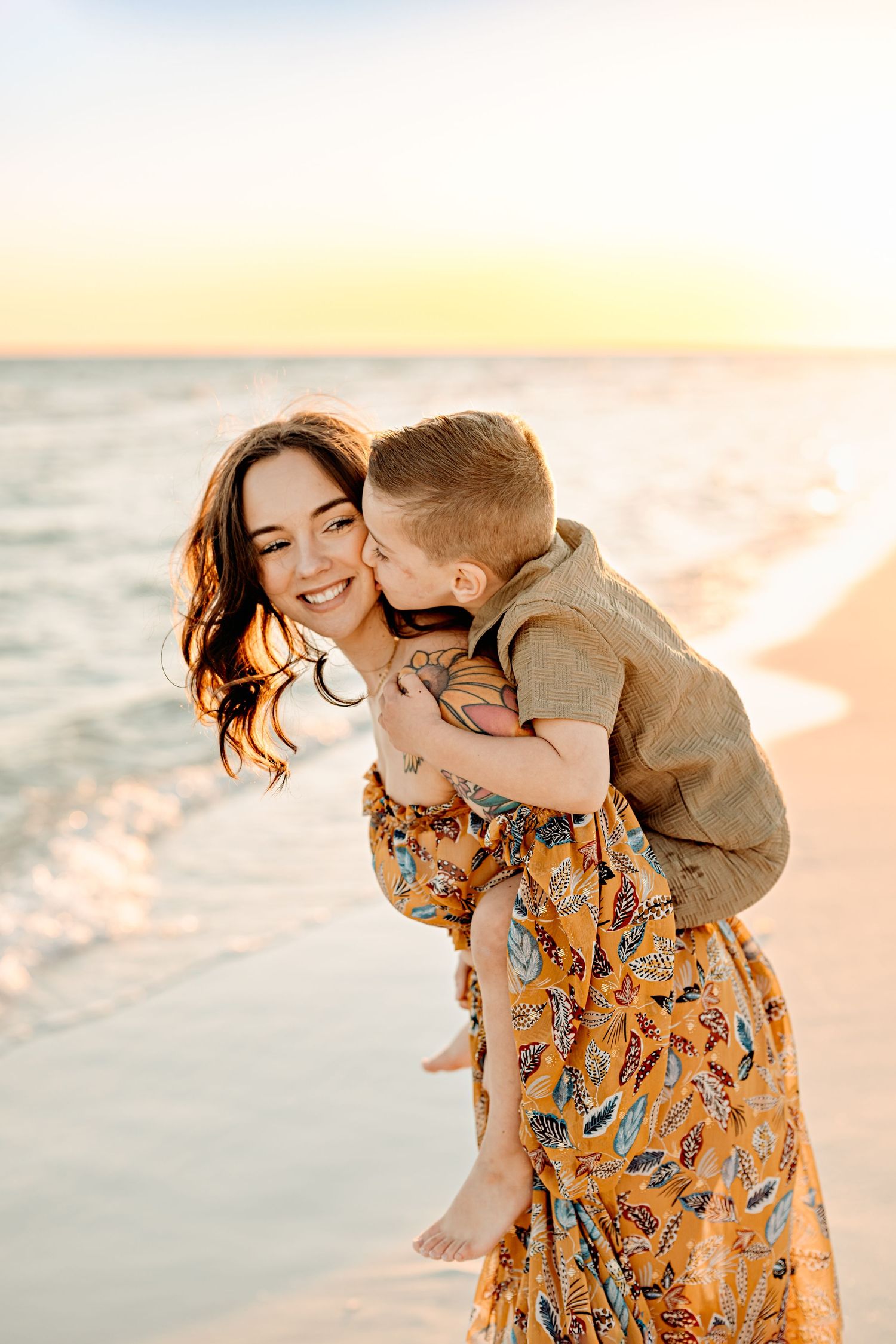 A smiling mother carrying her child on the back, both laughing and enjoying a sunny moment together.