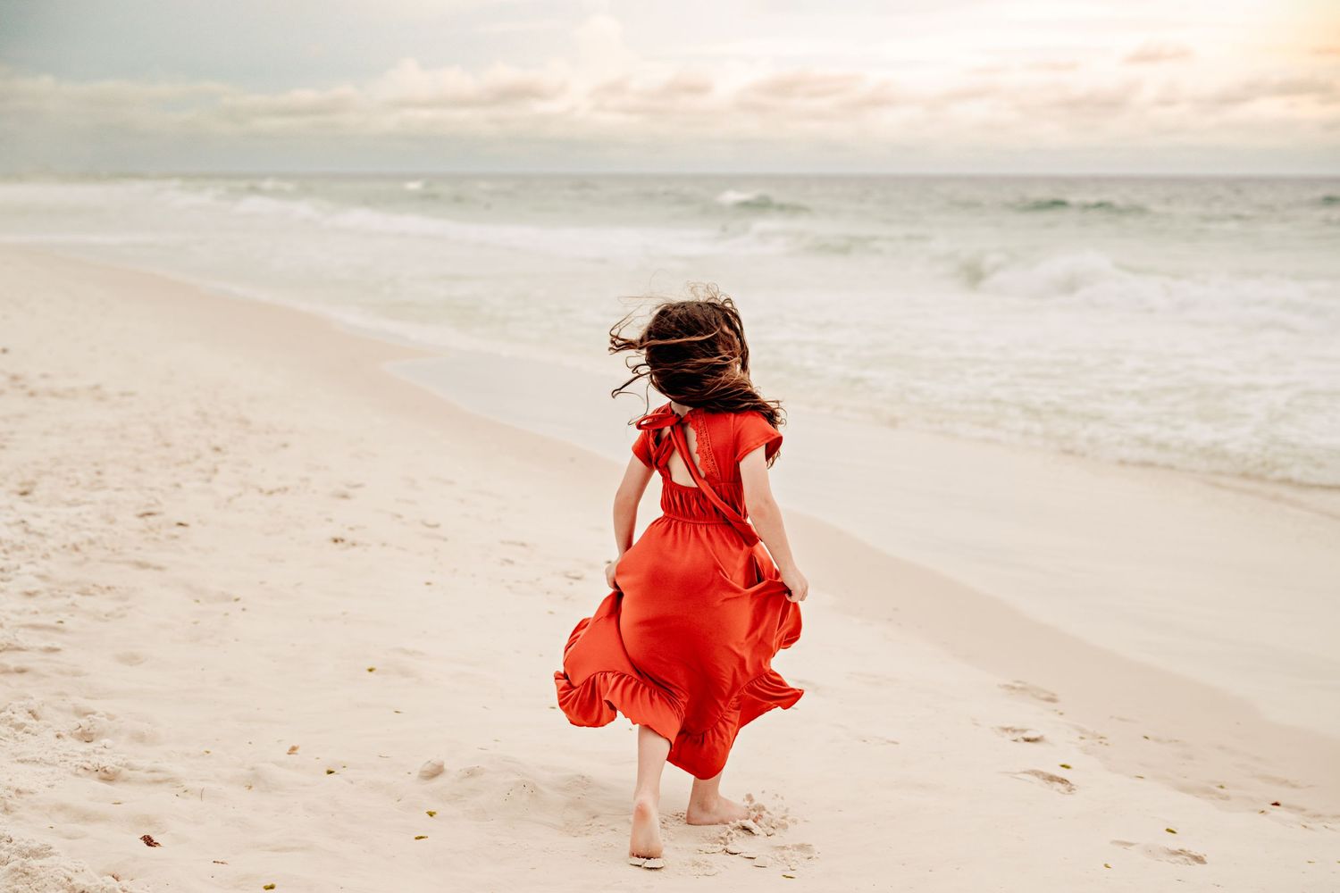 A girl running joyfully along the sandy beach with waves in the background.