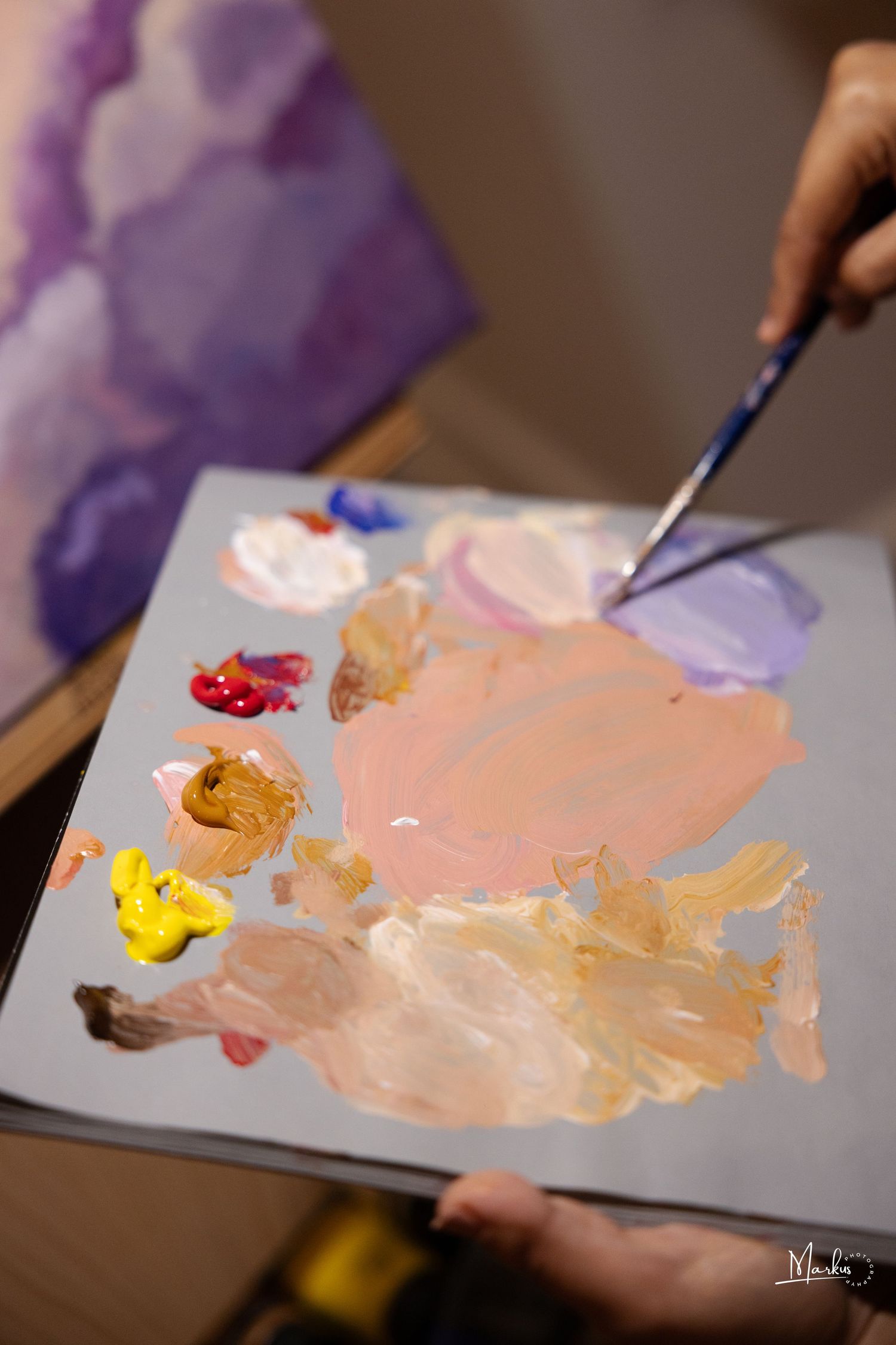 Artist's palette shows vibrant paint colors being mixed together on a white surface in natural lighting.