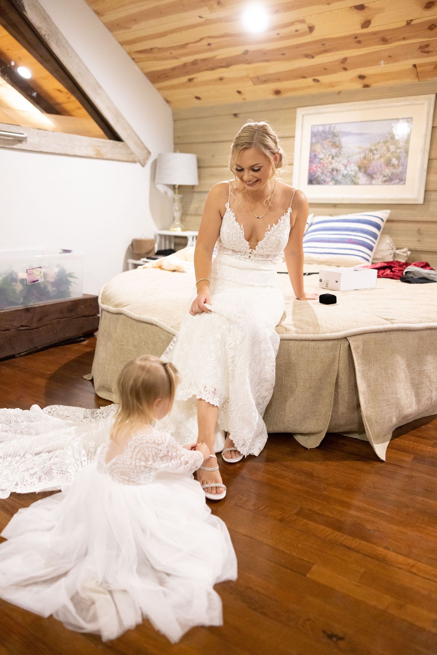 A tender moment between two people in white dresses sitting on a hardwood floor in a rustic bedroom.