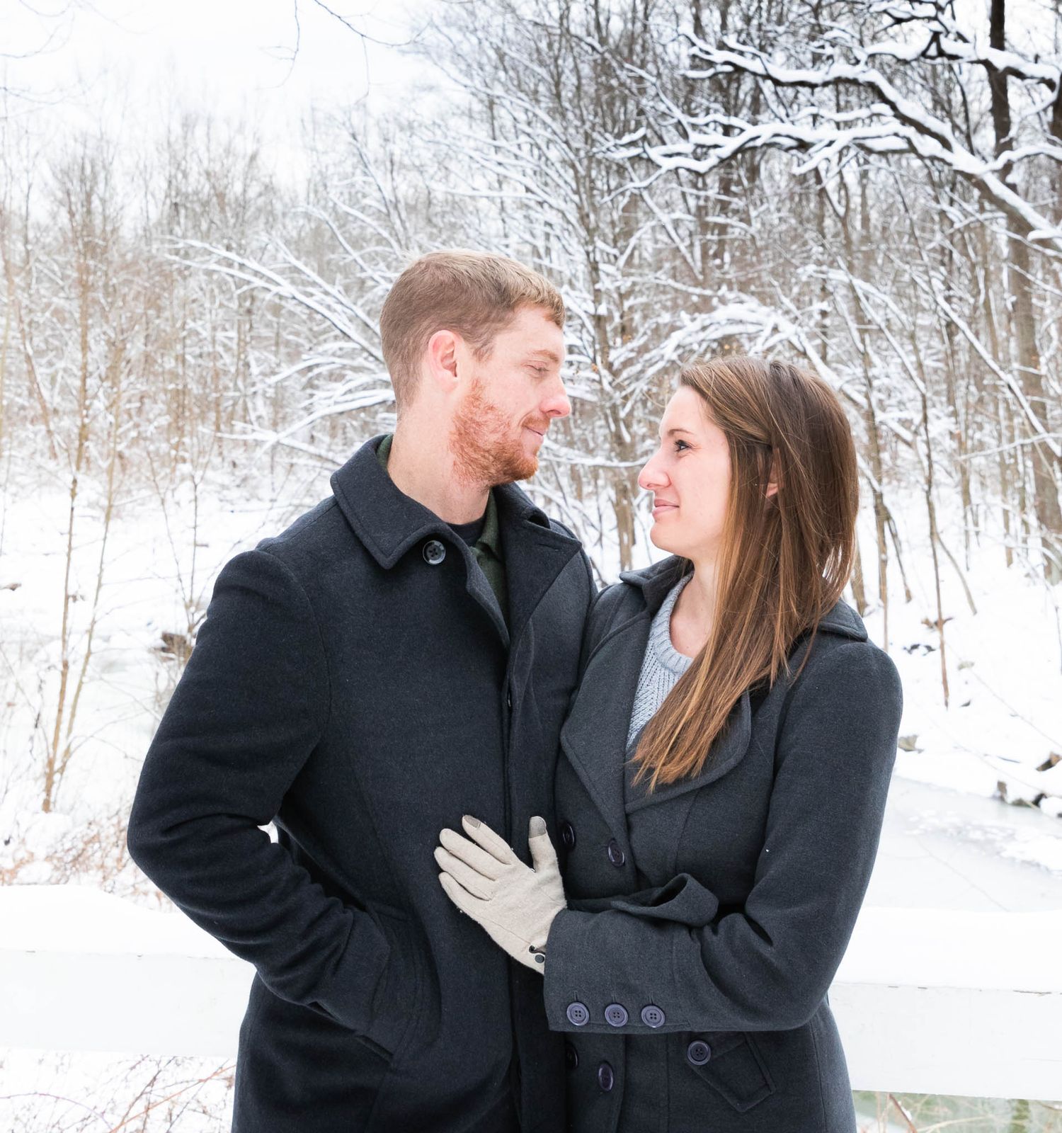 A couple in black coats shares romantic moments in a snowy winter forest setting.