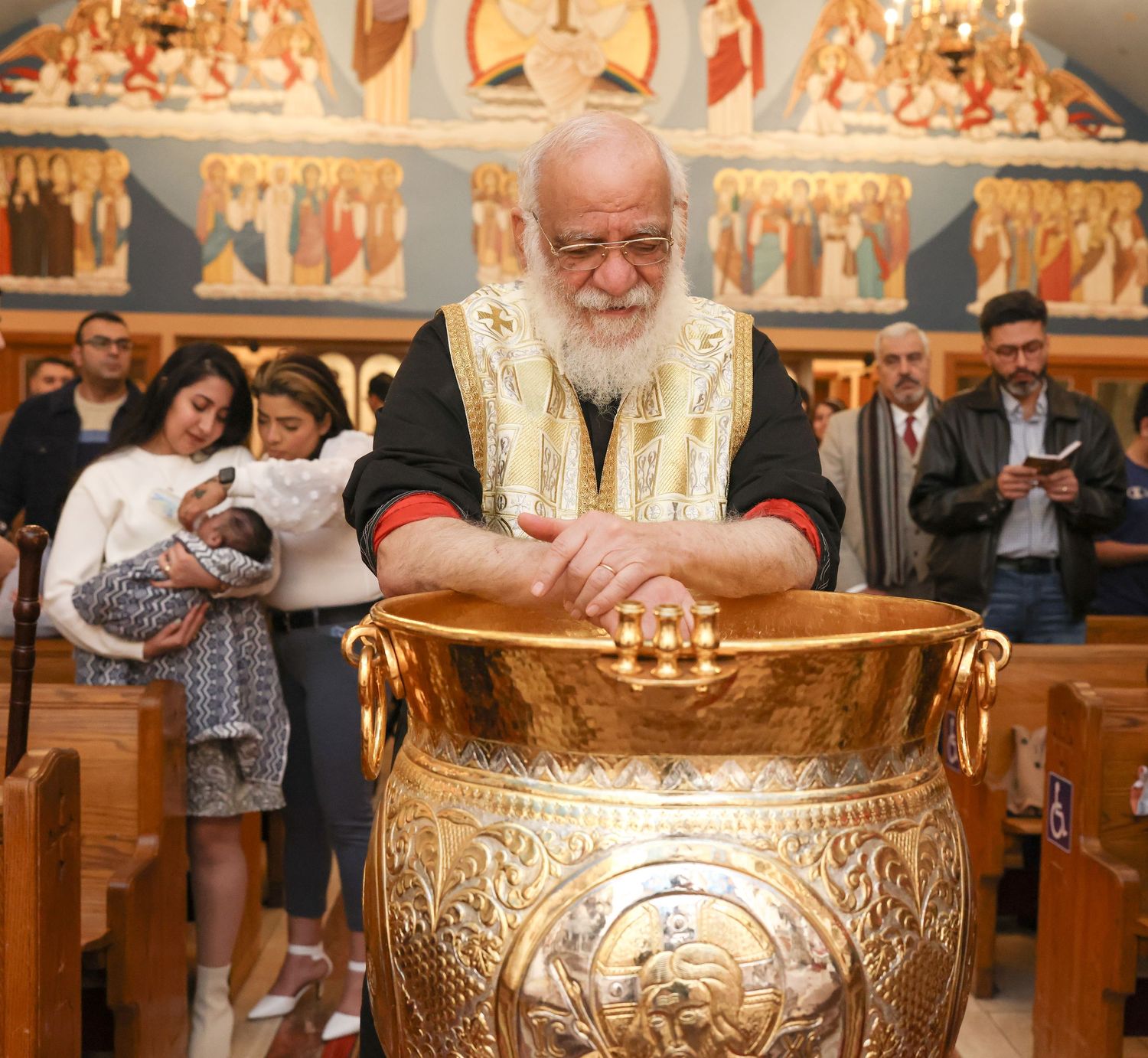 A person participates in an Orthodox Christian baptismal ceremony with ornate golden religious vessels and candles.
