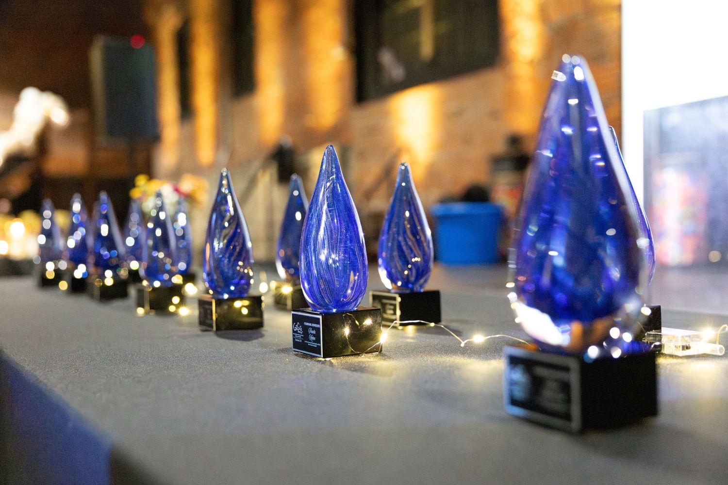 Blue glass art sculptures displayed in a row on a gallery shelf with dramatic lighting.