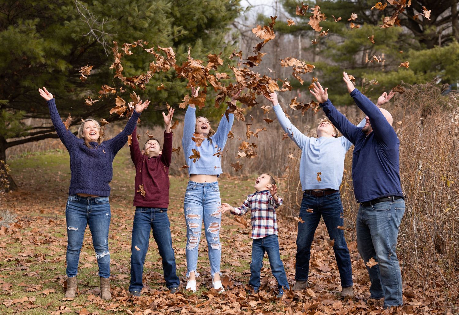 A group of people standing in autumn leaves raise their arms in celebration against a natural outdoor backdrop.