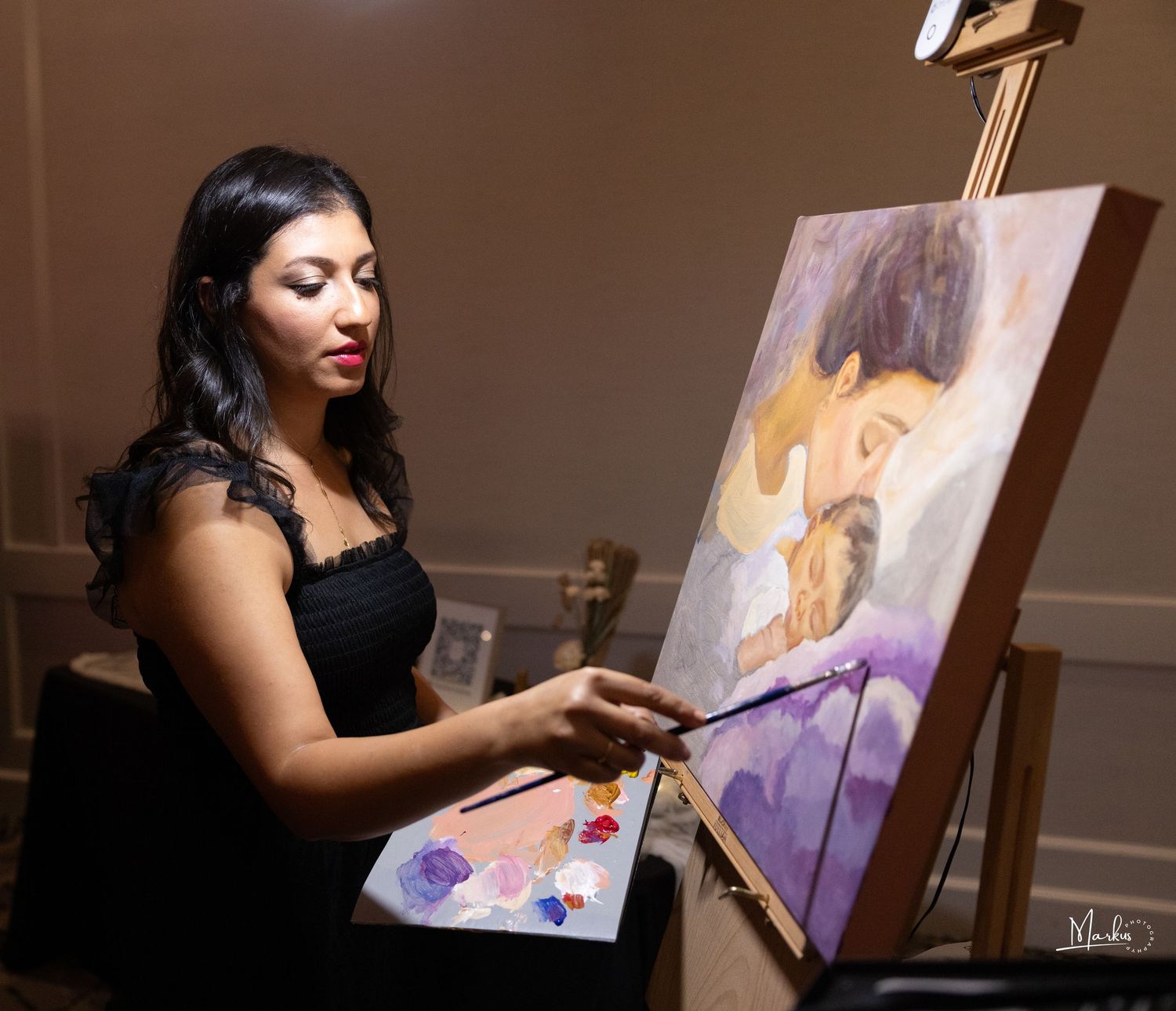 Artist in a black dress creates vibrant abstract painting on canvas at wooden easel in studio setting.