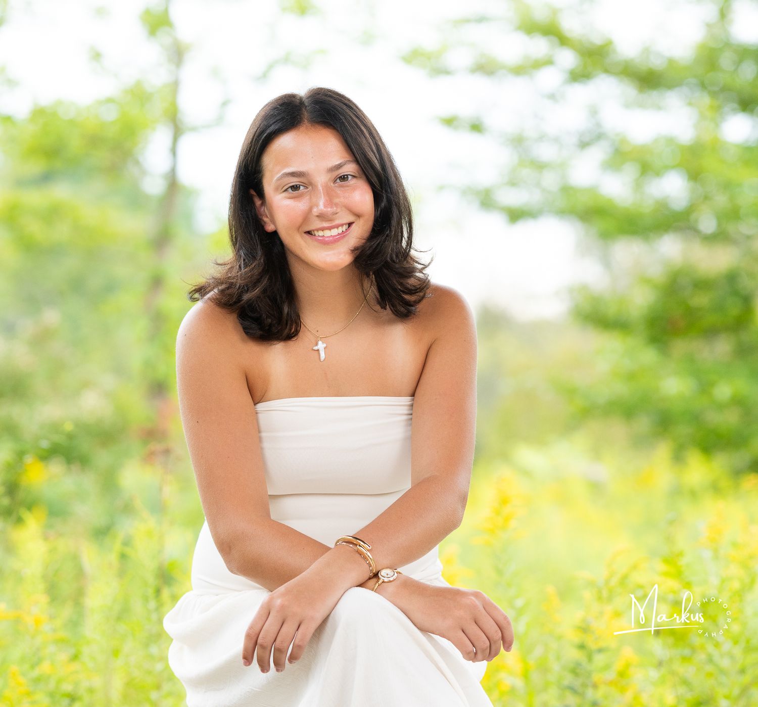 Young woman in white strapless dress smiling in a sunny field of yellow wildflowers for senior portrait.