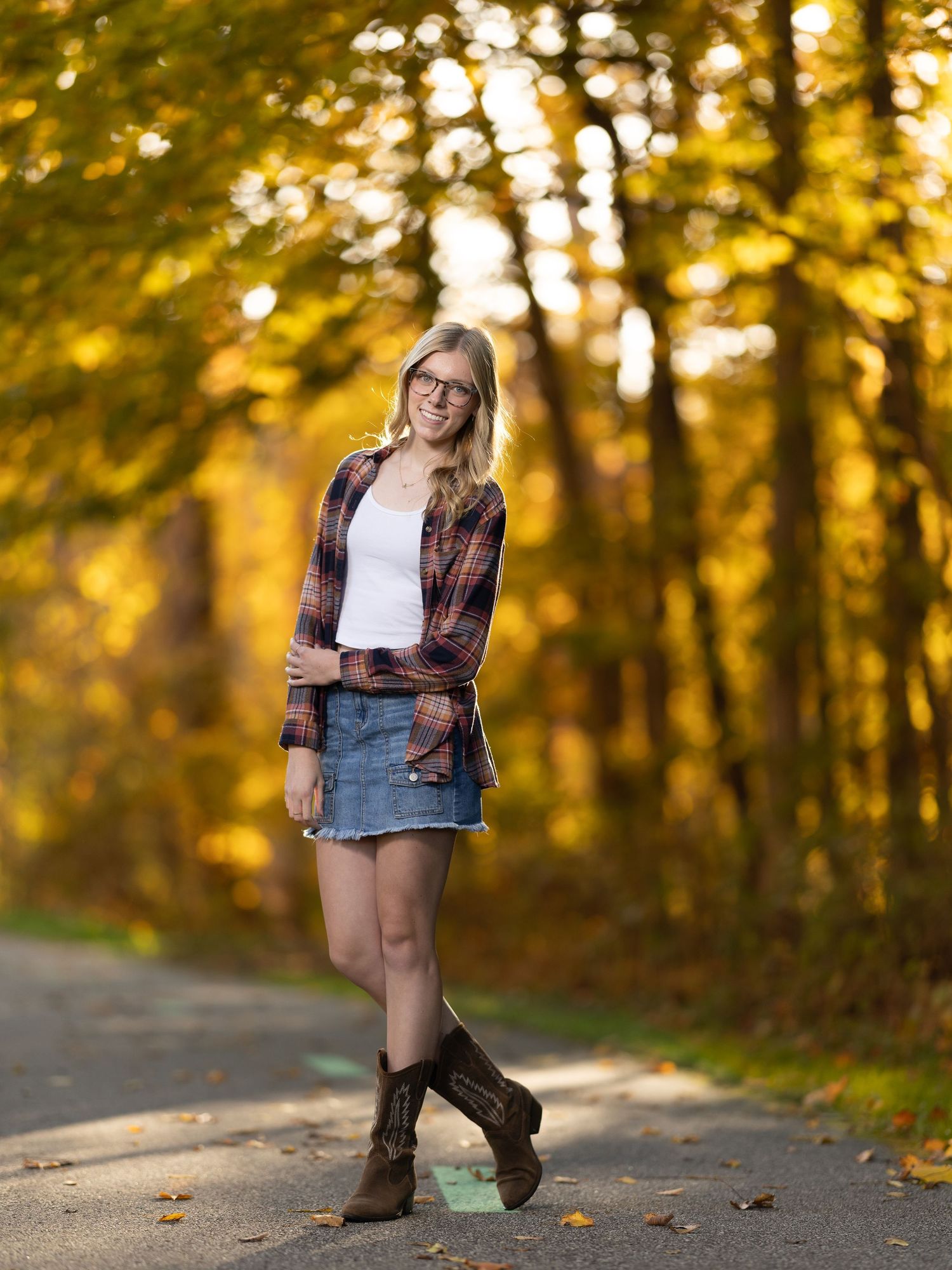Person in plaid shirt and boots walks along autumn path with golden sunlight filtering through trees.