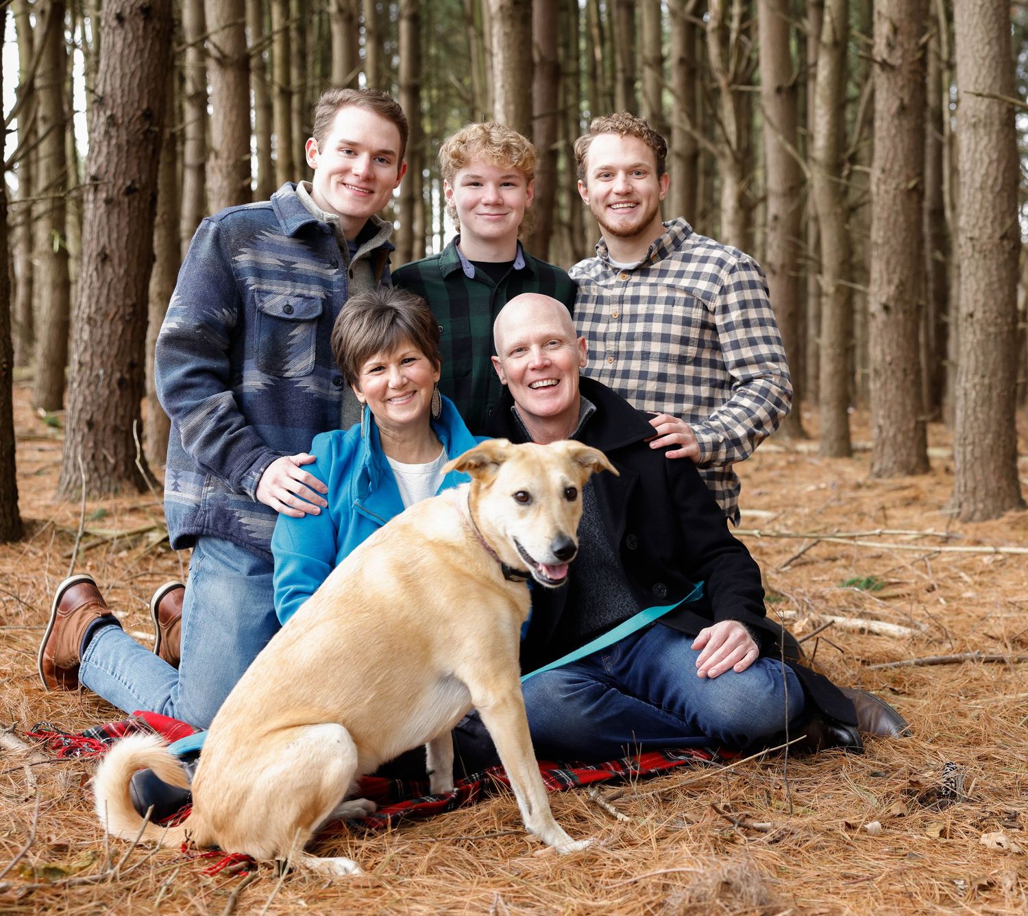 Family group with dog posing together on pine needle covered forest floor.