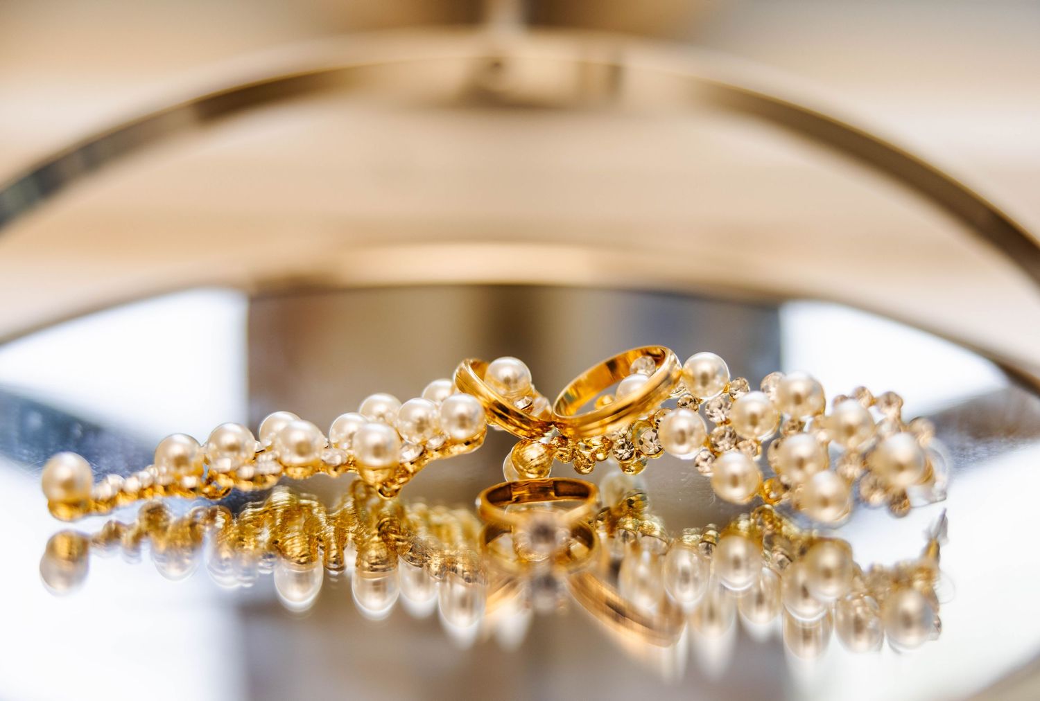 Delicate pearl and gold bridal jewelry pieces arranged in a row on a reflective surface.
