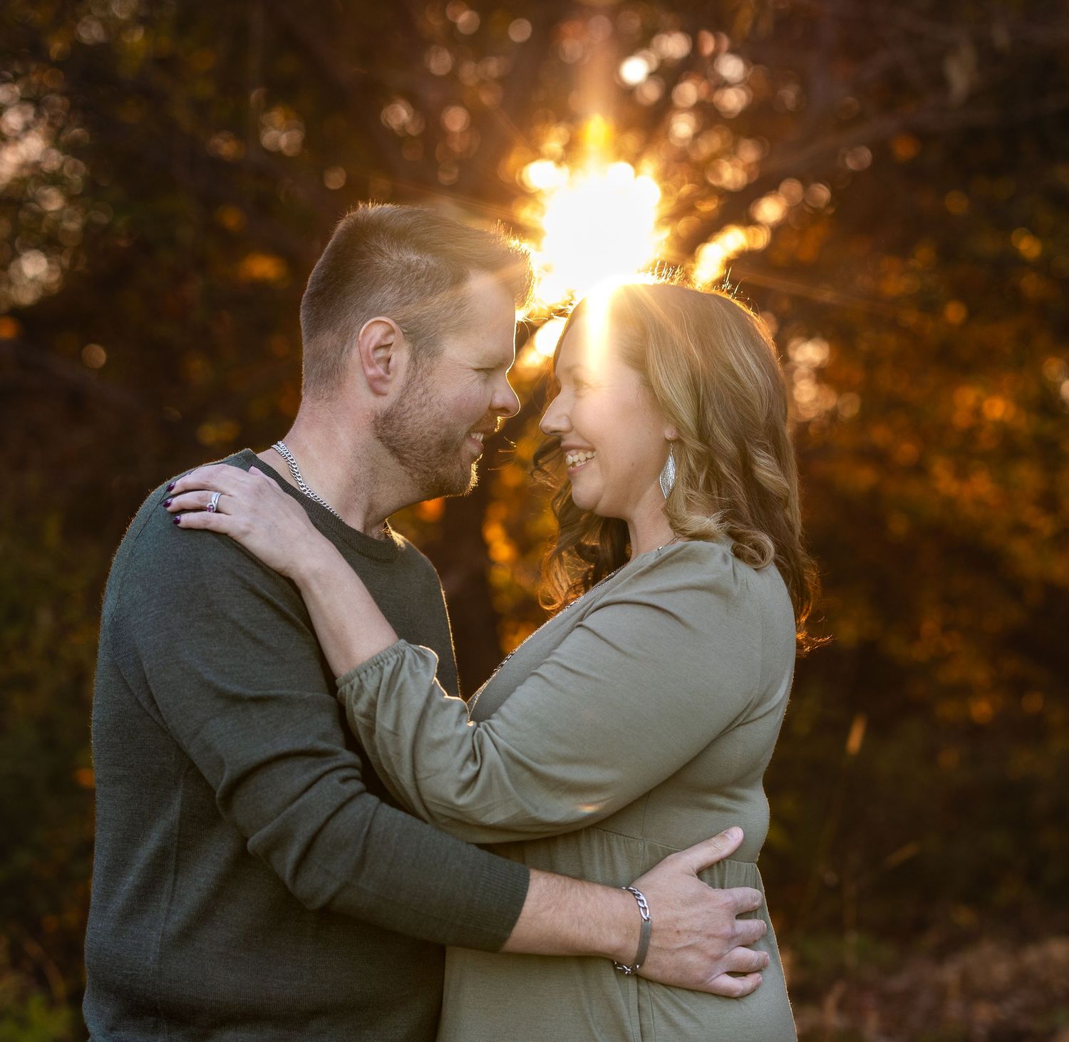 Romantic couple embracing at sunset with golden bokeh lighting in background.