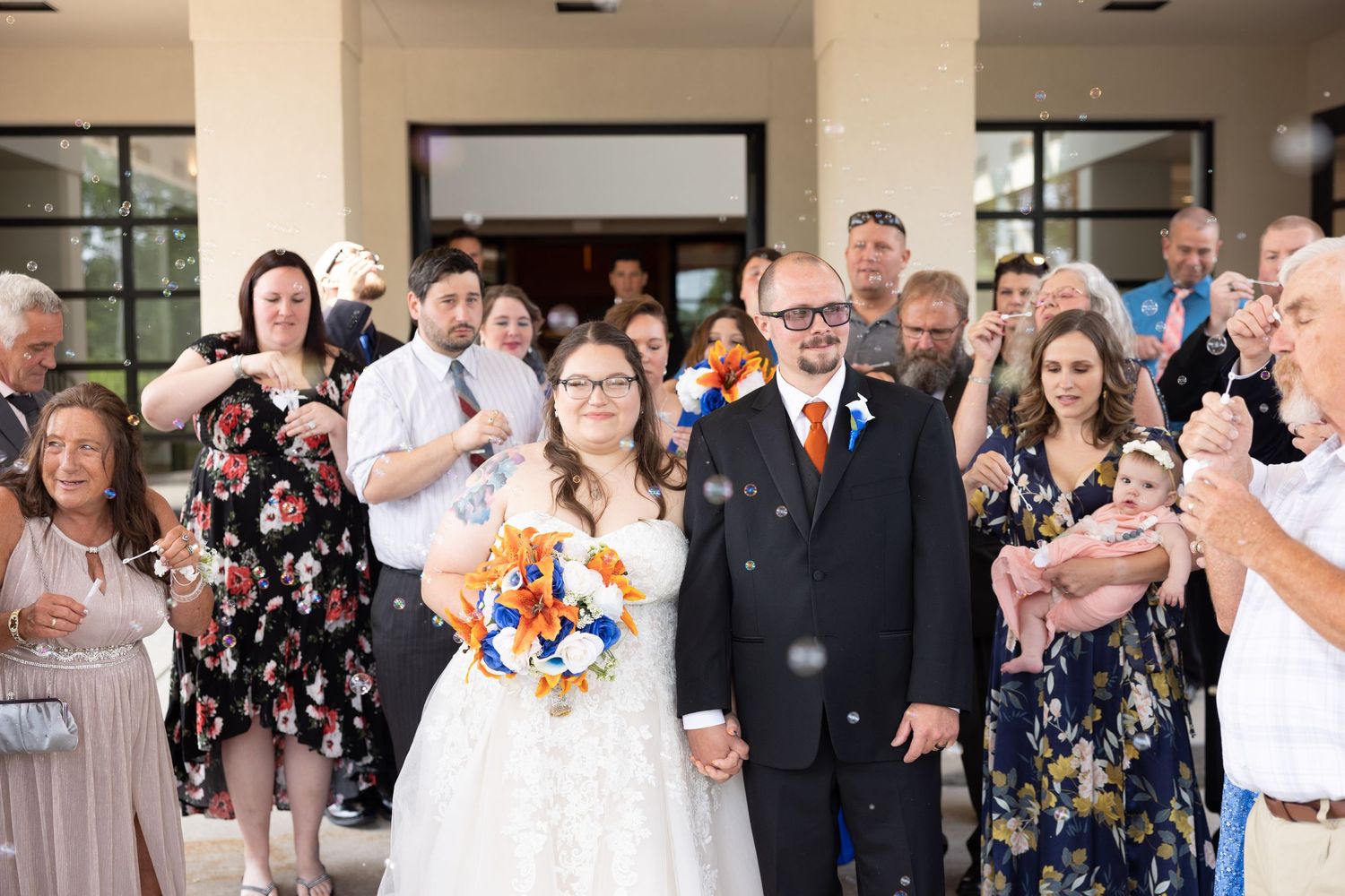 Wedding guests smile and applaud during an indoor reception celebration.