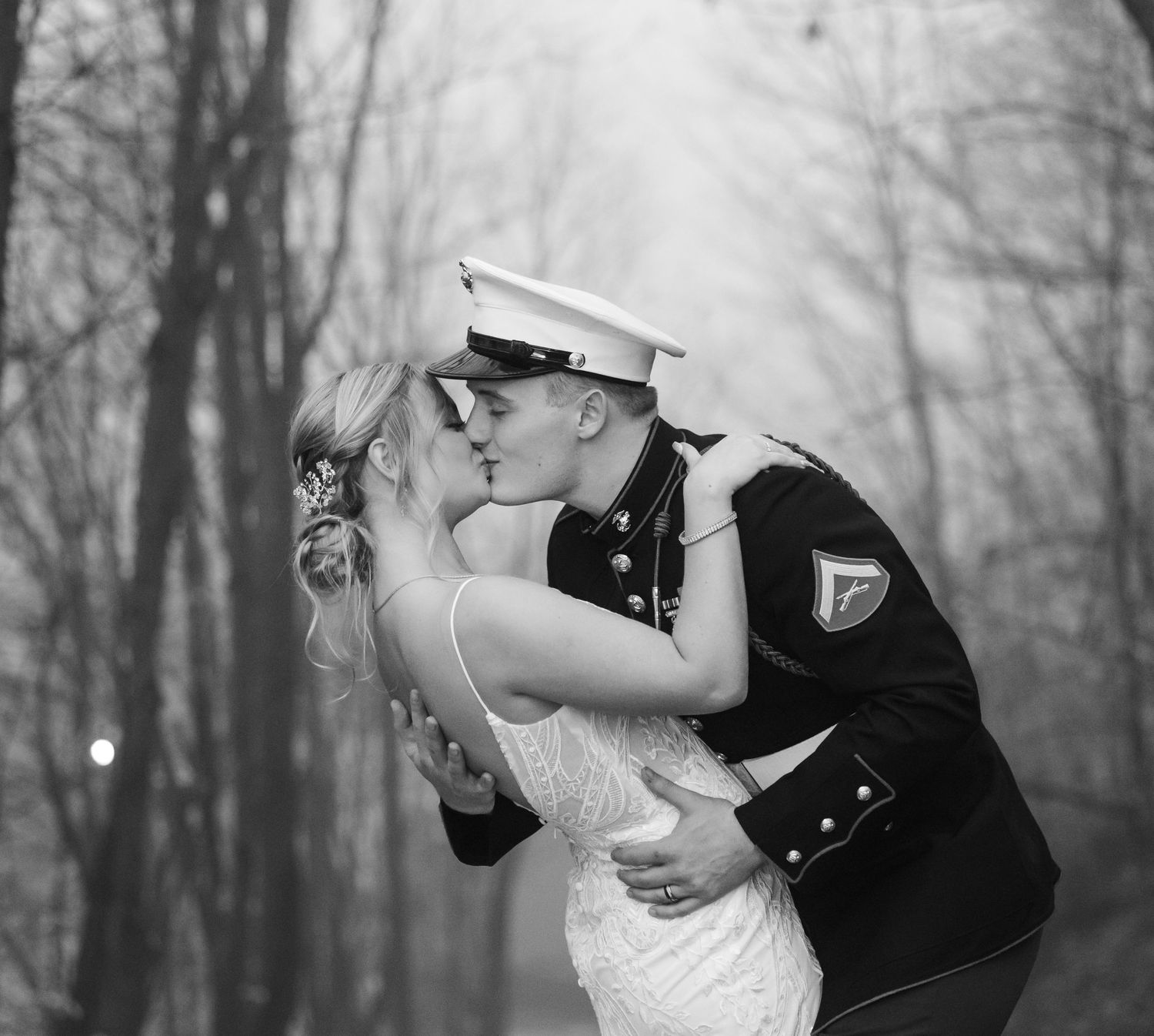A romantic black and white photo of a couple sharing a kiss outdoors in formal dress and military uniform.