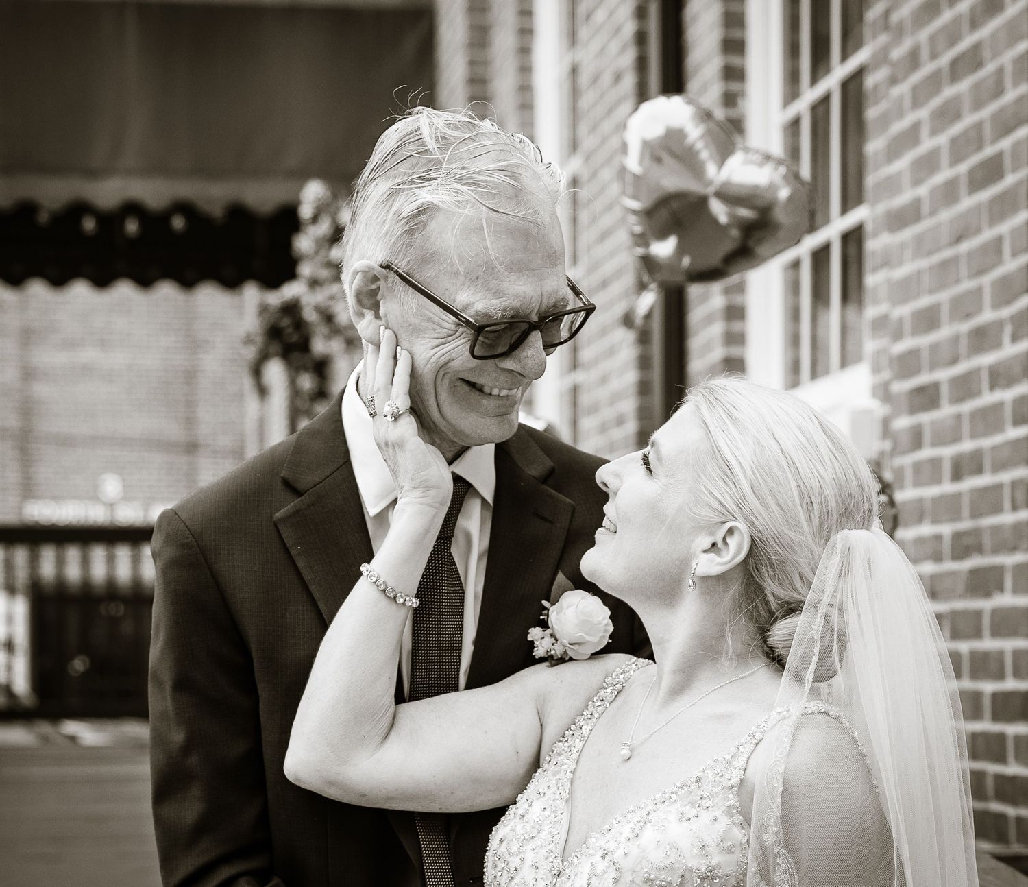 Black and white photo of a smiling bride tenderly touching an older mans face at a wedding.