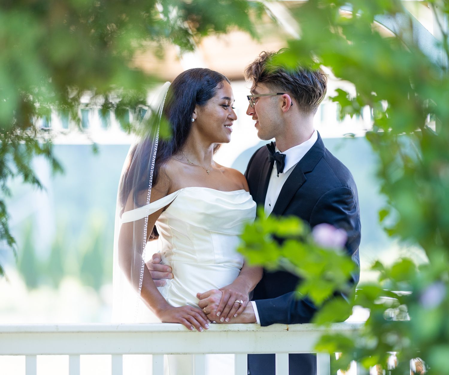 A romantic wedding couple embraces under lush green trees during an outdoor summer photo session.