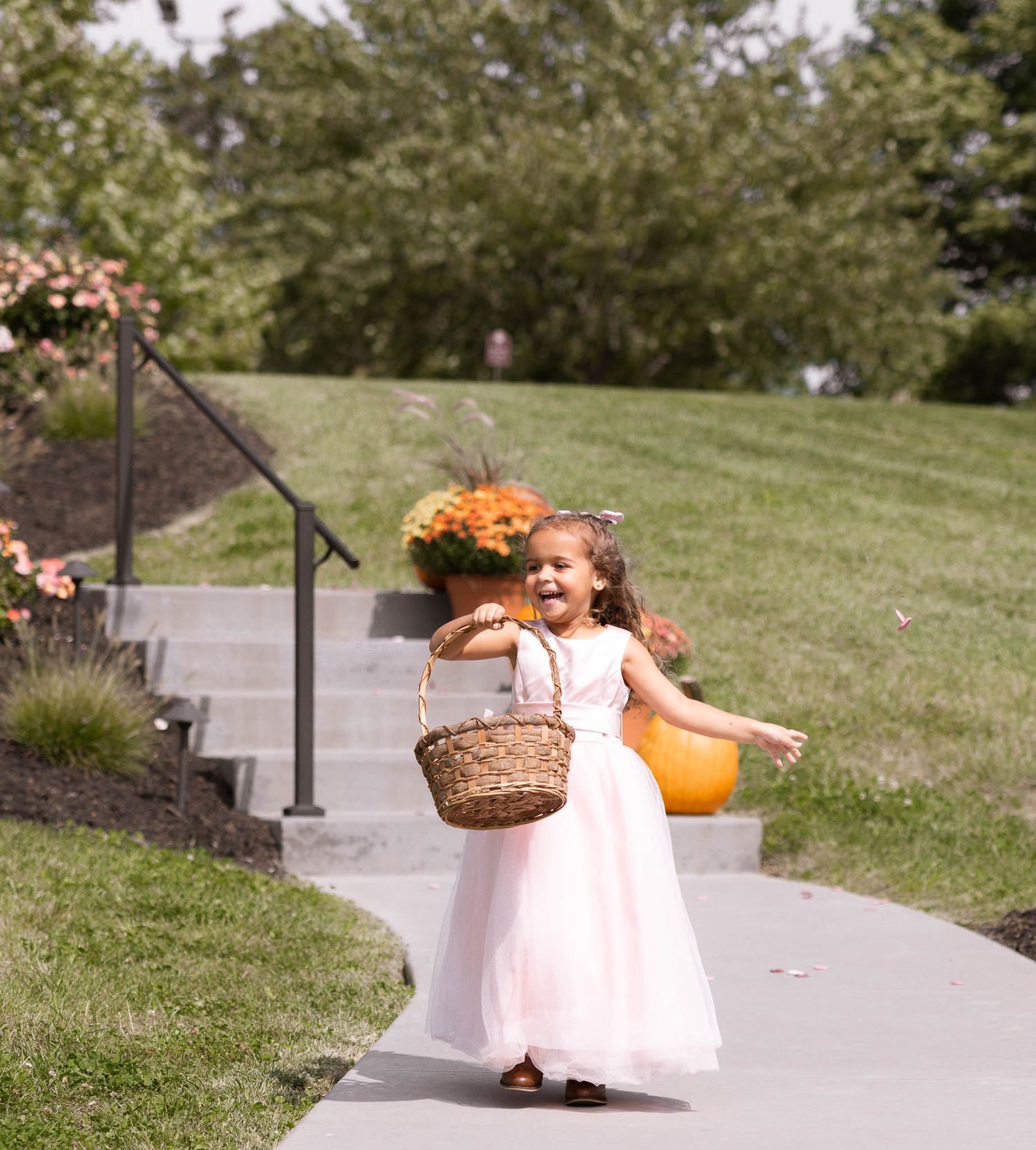 A figure in a white dress spins around on a concrete pathway surrounded by green grass and autumn decorations.