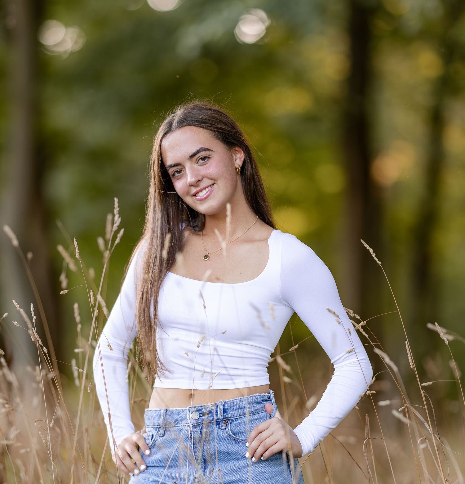 Senior portraits in white crop top and jeans amid tall grass.