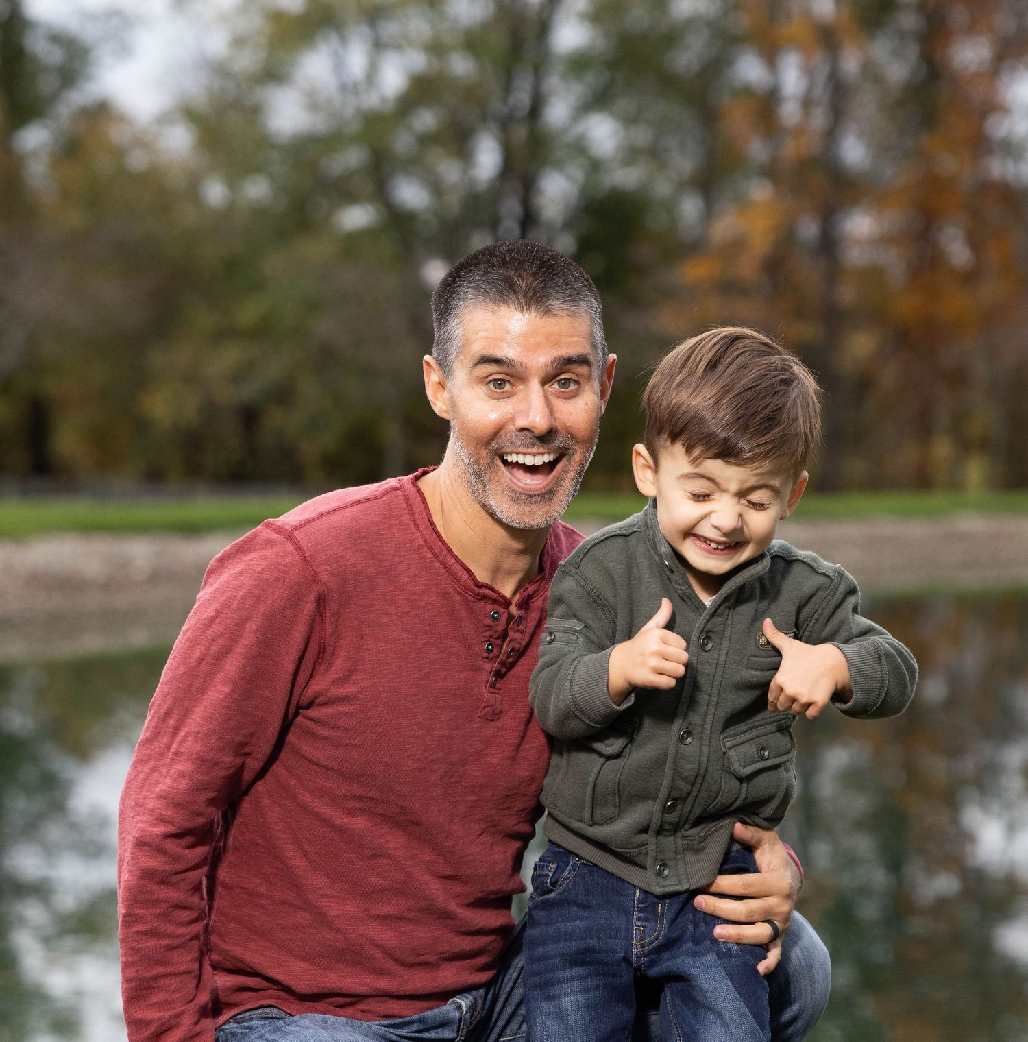 Two people sitting together on a bench near a pond during autumn, sharing joyful laughter and smiles.