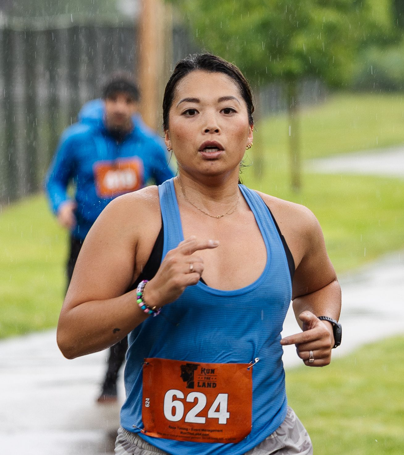 Runner in blue tank top and bib number 624 participates in an outdoor race on a cloudy day.