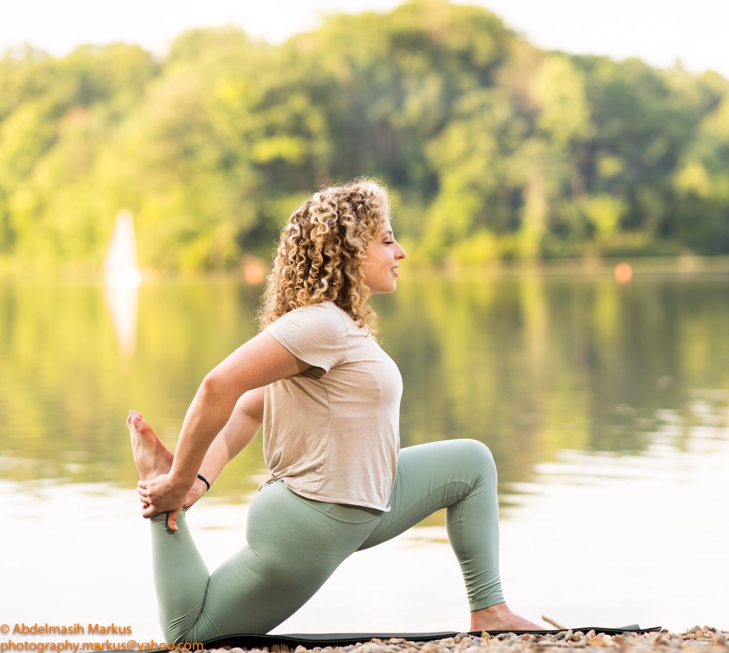 A pregnant woman in yoga attire practices stretching exercises by a serene lake during golden hour.
