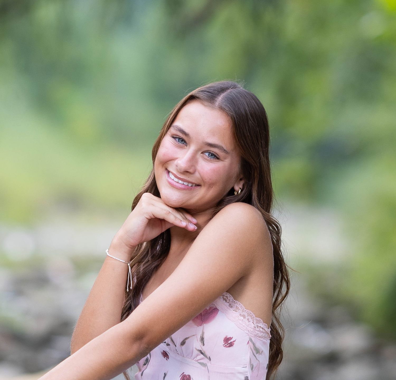 Person in a floral dress poses outdoors against a soft blurred natural background.