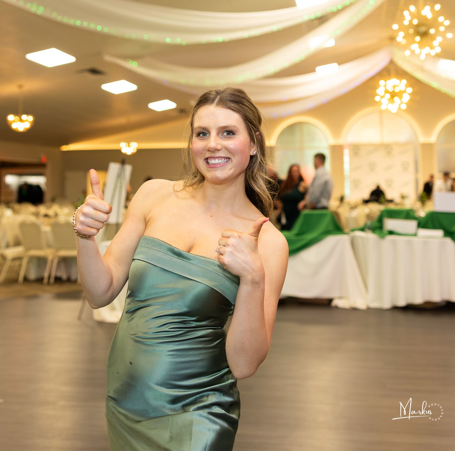 A woman in a teal satin dress dances gracefully on a reception hall dance floor with decorative lighting.