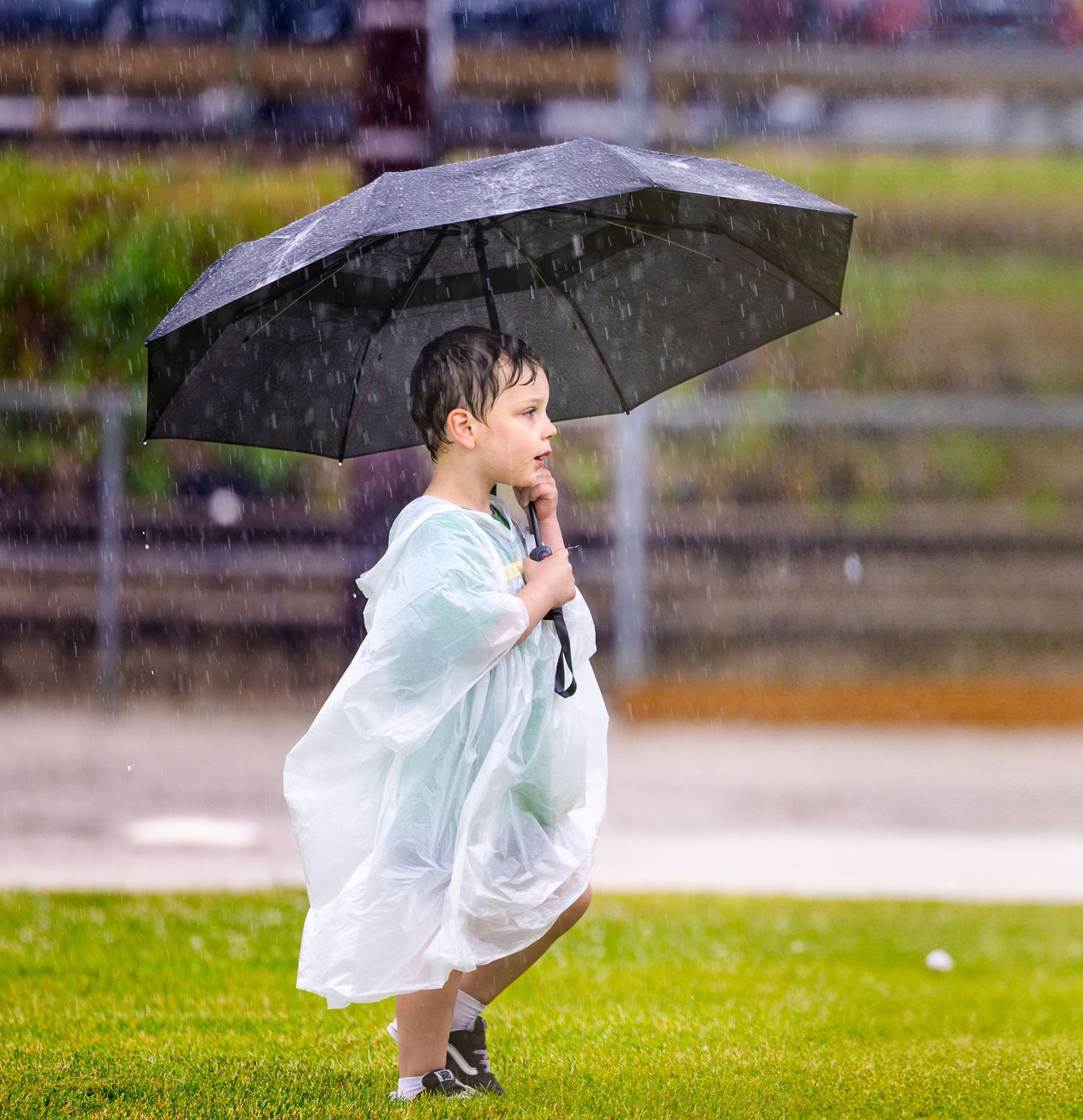 A child in a light raincoat runs through a rainy field while holding a black umbrella.